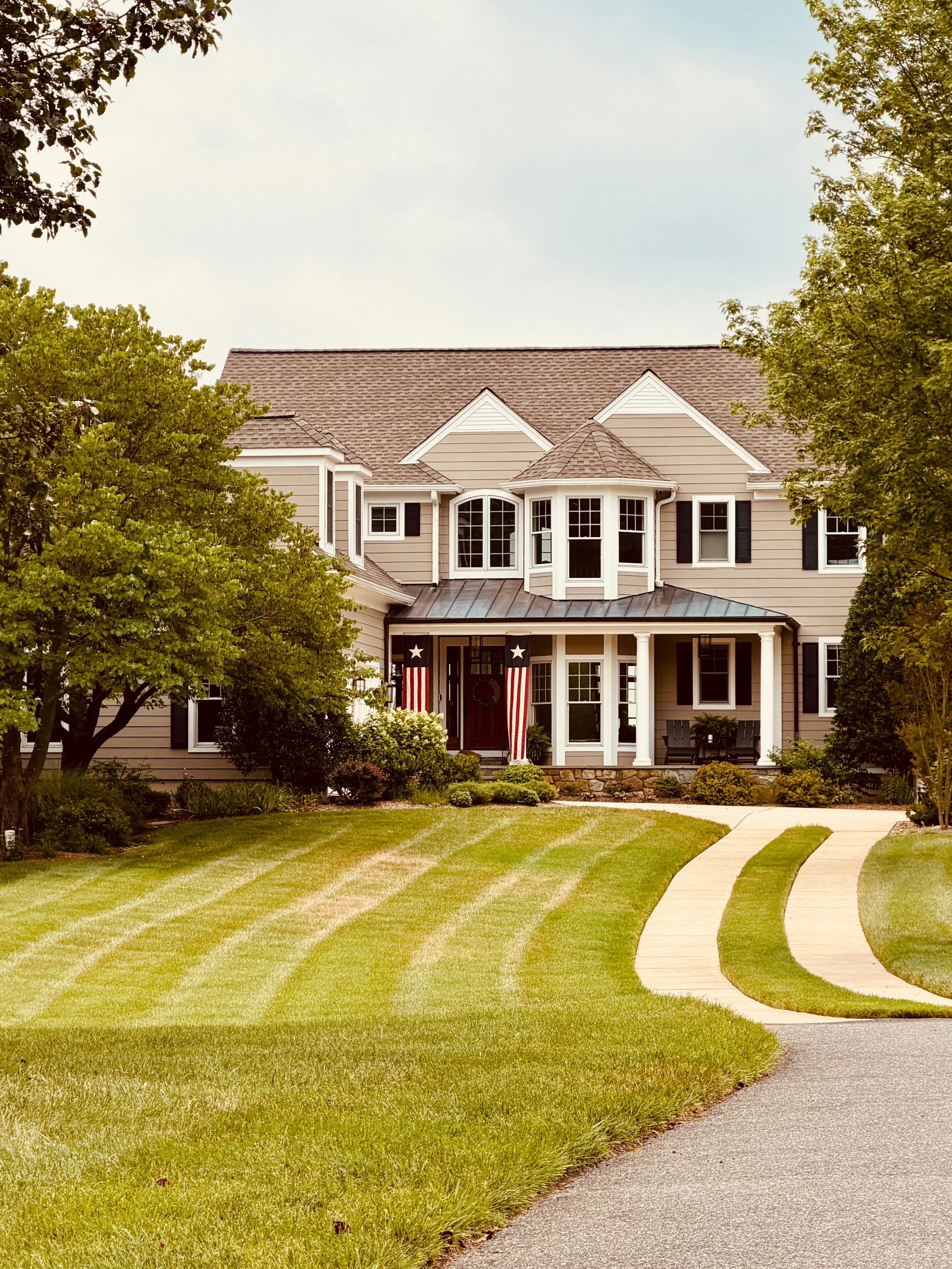 A large two storey house with pale siding, a columned front porch and an autumn tree in the front garden