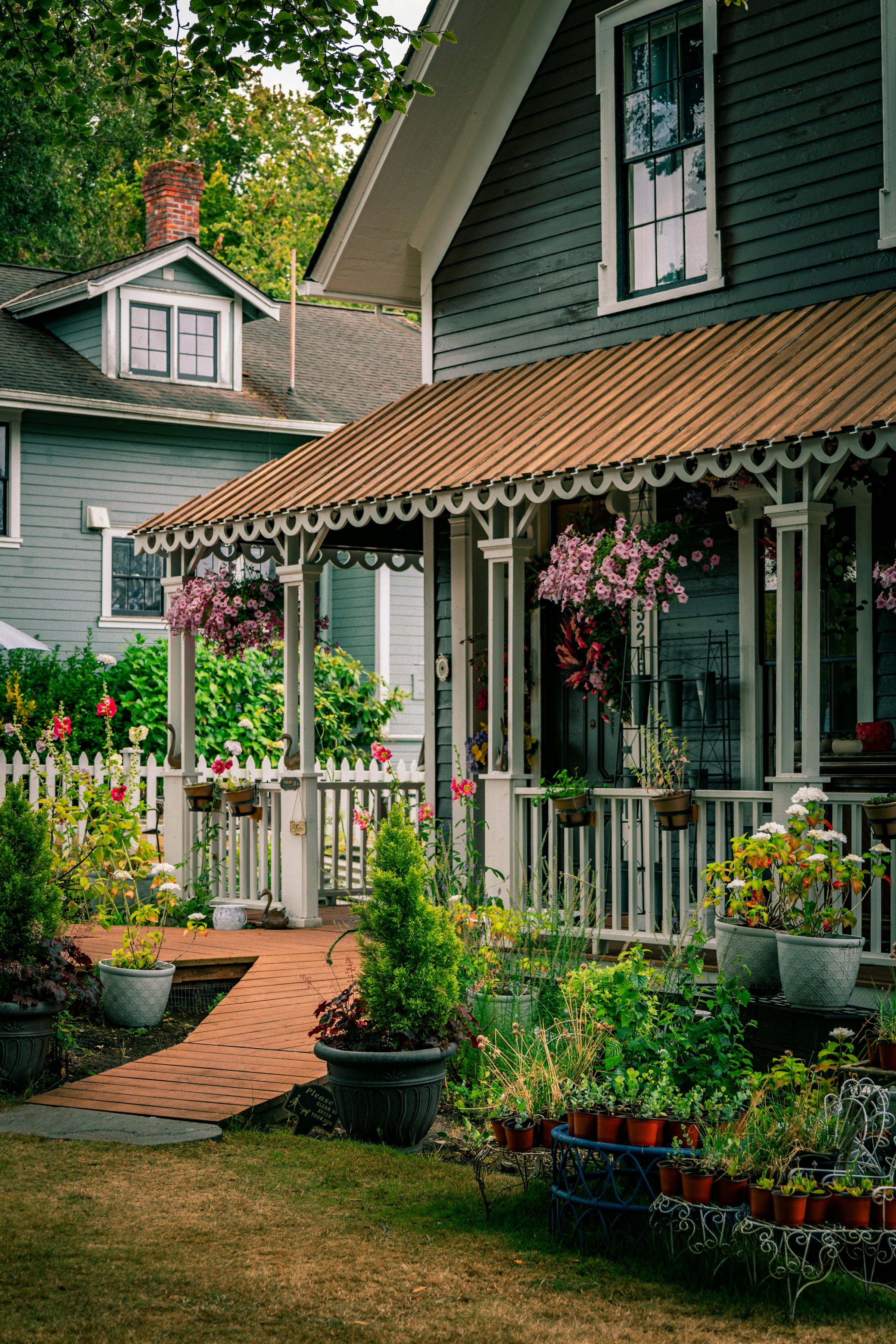 A green painted Victorian porch with a striped awning and flowering plants along the railing