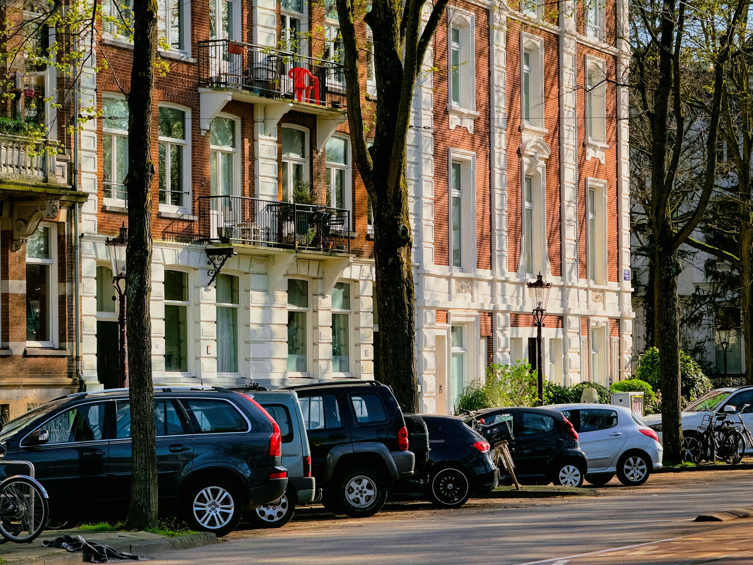 A row of ornate Victorian townhouses in varied colours with cars parked along the street