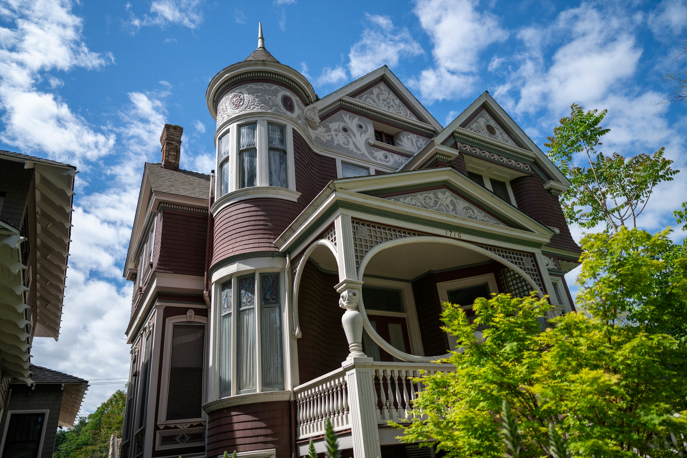 An ornate Victorian house with a corner turret and decorative gable trim against a blue sky.