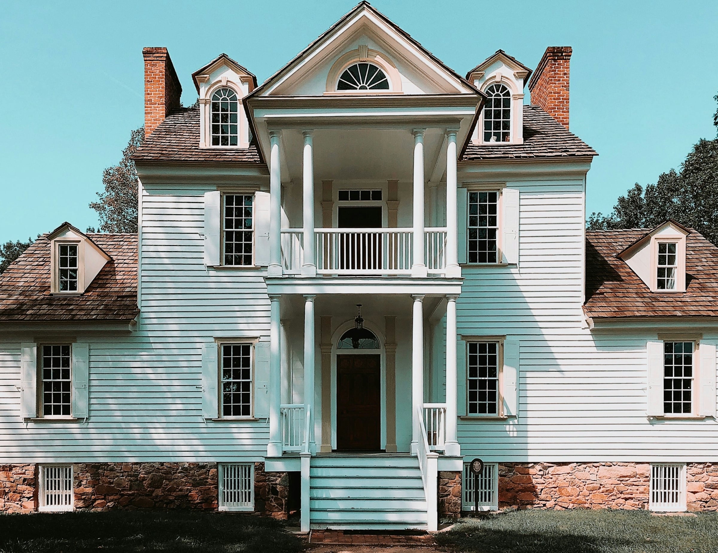 A white two-story colonial house with a columned double porch, dormer windows and a brick foundation.