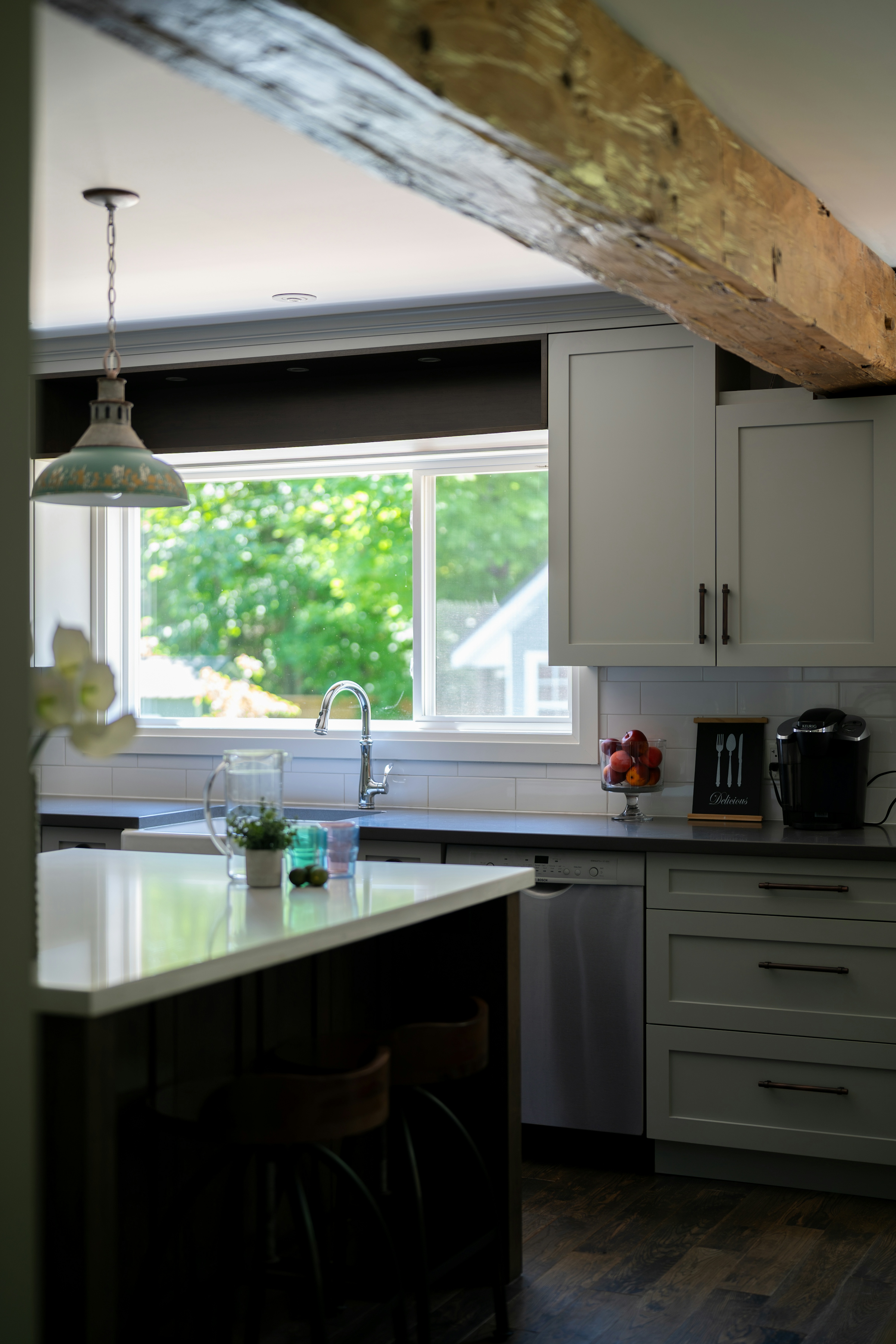 A white kitchen with a window above the sink and herbs growing in pots on the sill
