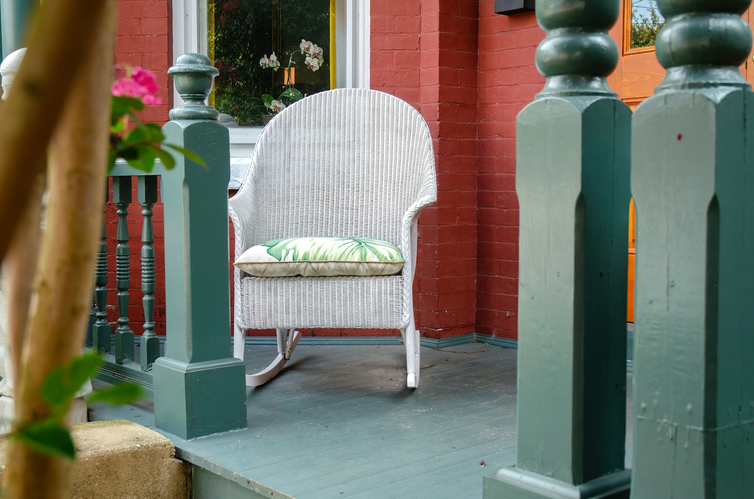 A white wicker rocking chair with a cushion on a painted porch beside a green post
