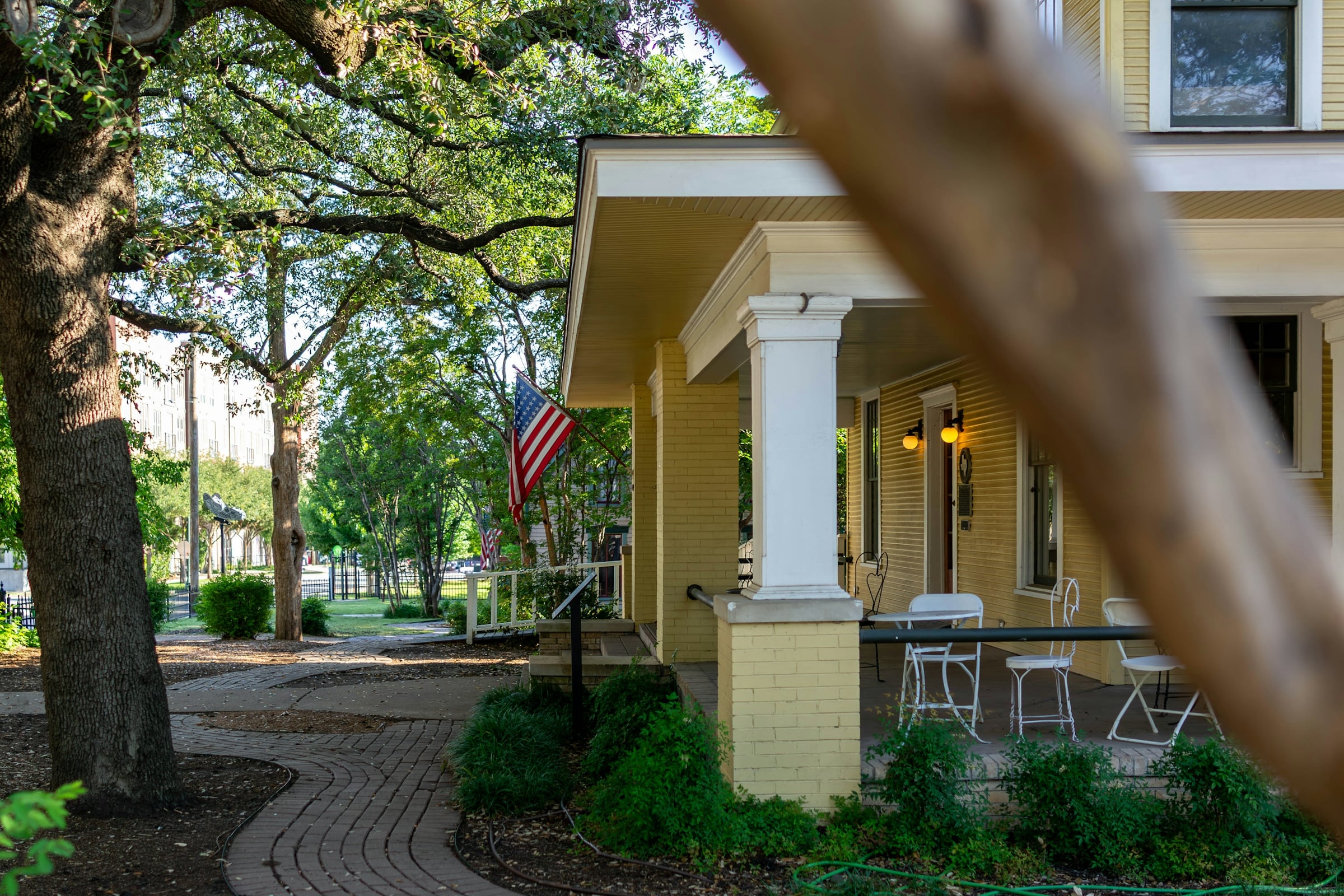 A pale yellow house with white columns on a tree lined street with an American flag by the door