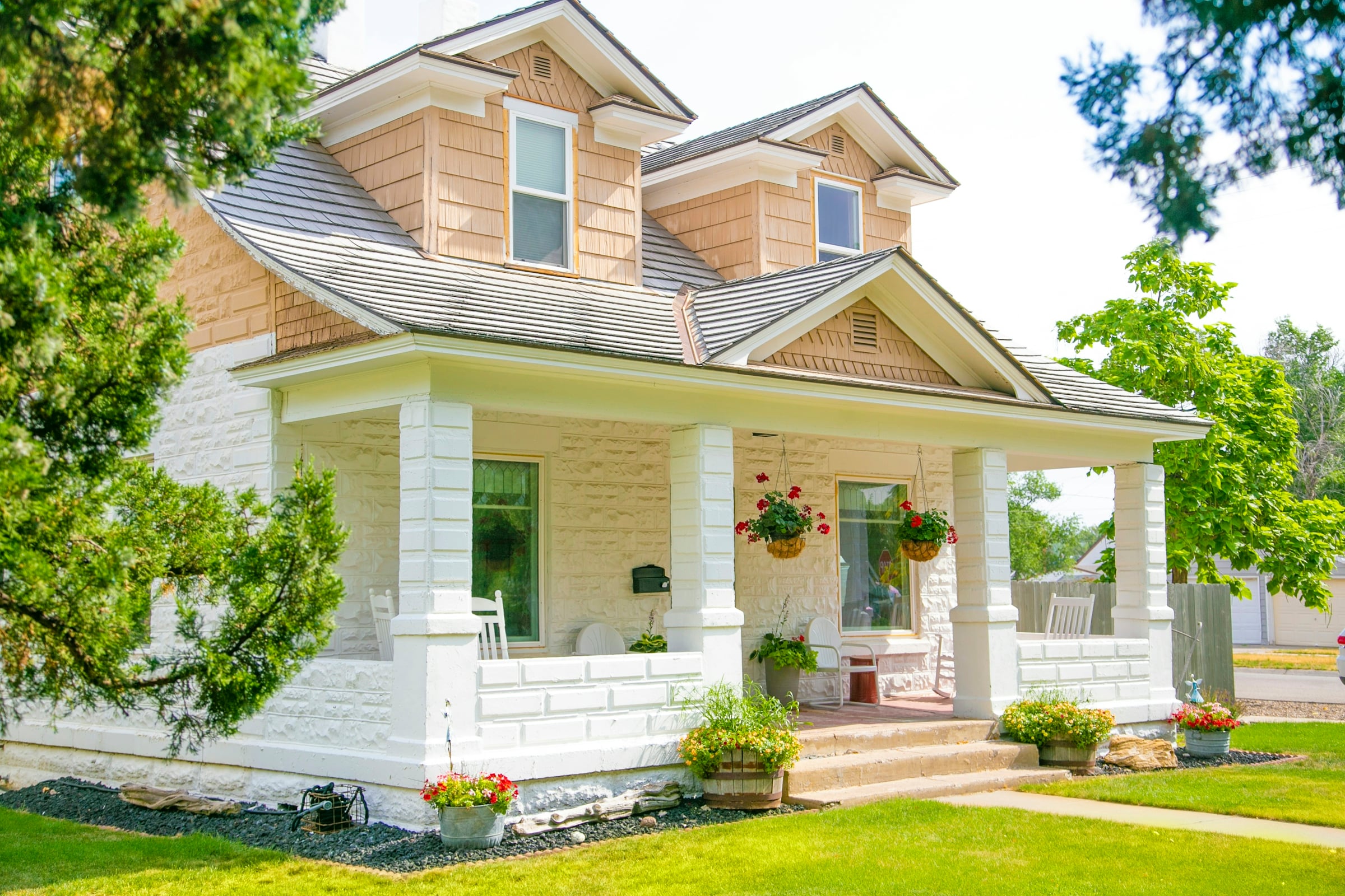 A pale yellow Victorian farmhouse with a wraparound covered porch and a steep gabled roof