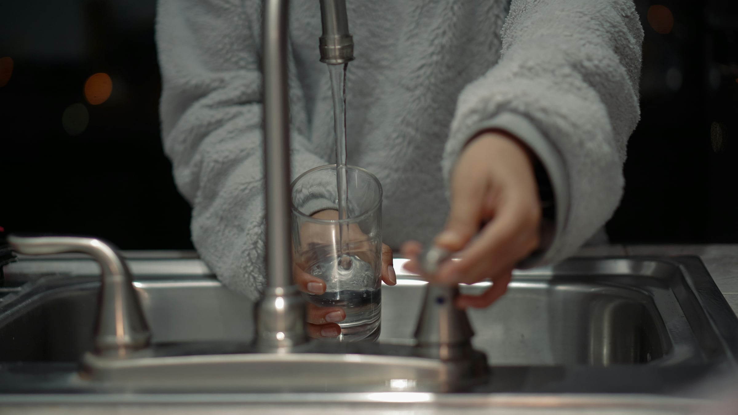 Person filling a glass at a kitchen faucet, representing checking tap water and service line material in an older home