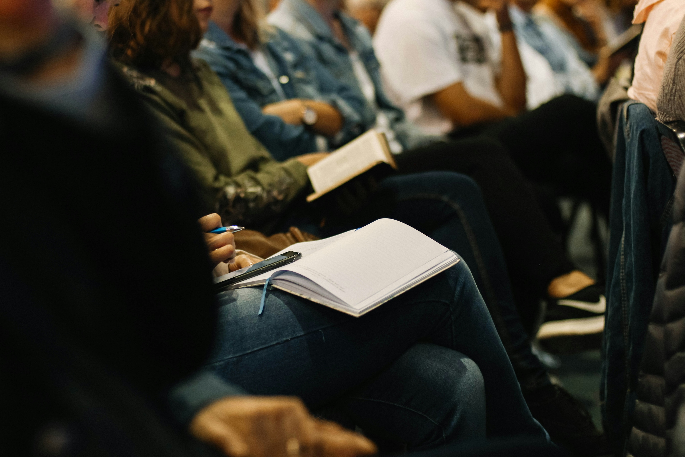 Audience members seated in rows writing in notebooks at a public meeting