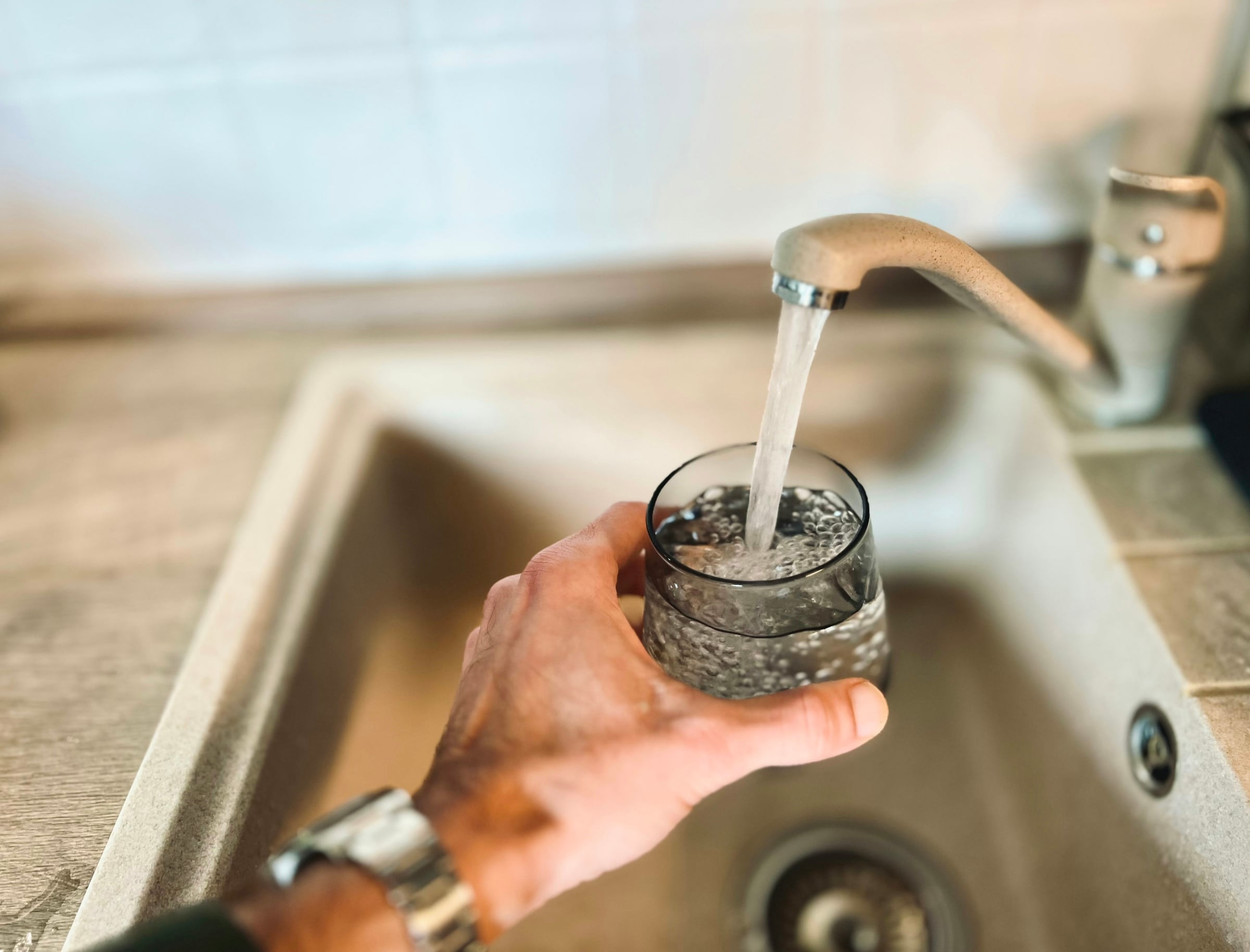 Hand holding a glass under a running kitchen faucet, representing checking tap water quality before buying a home