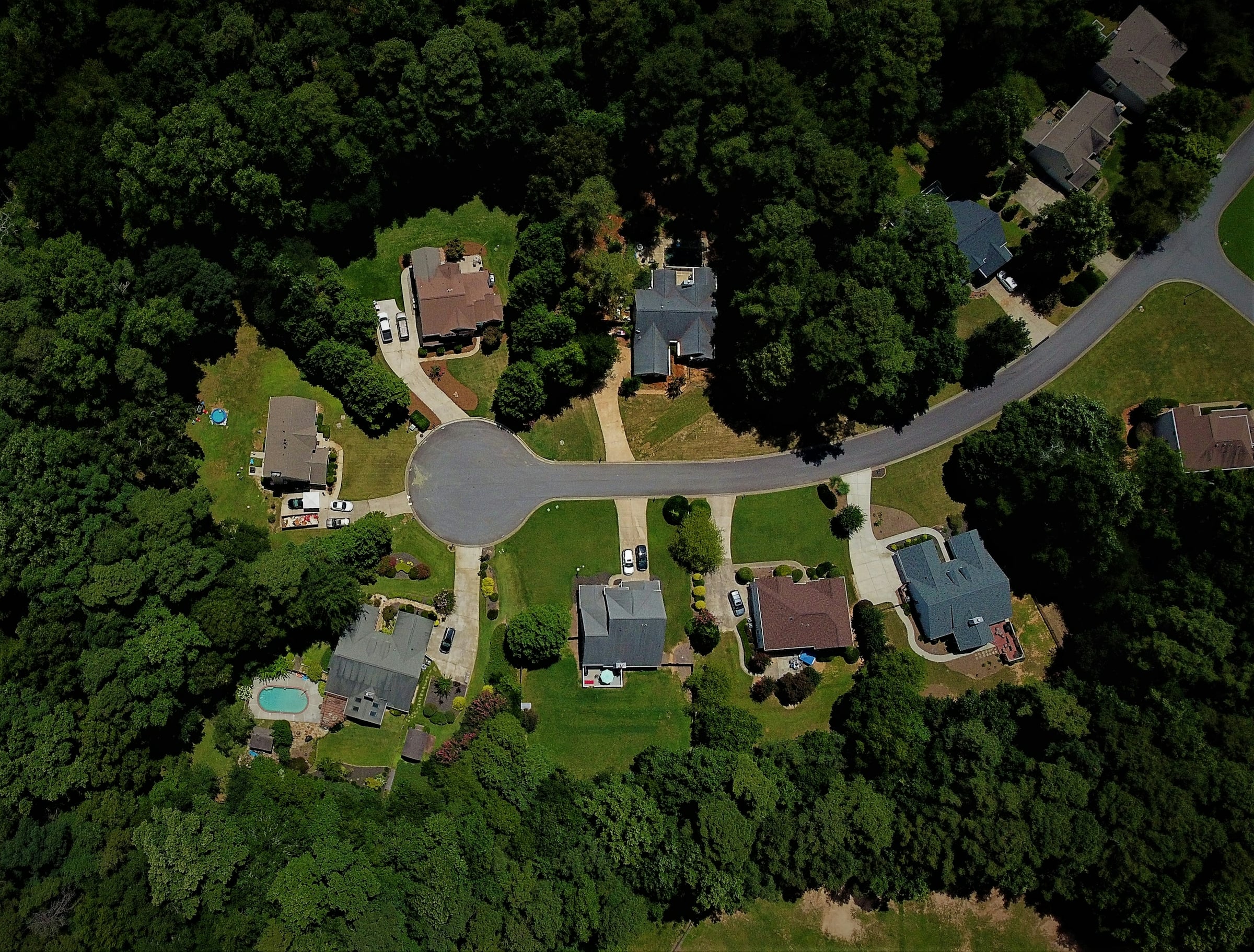 Aerial view of a wooded suburban cul-de-sac with detached homes and a backyard pool