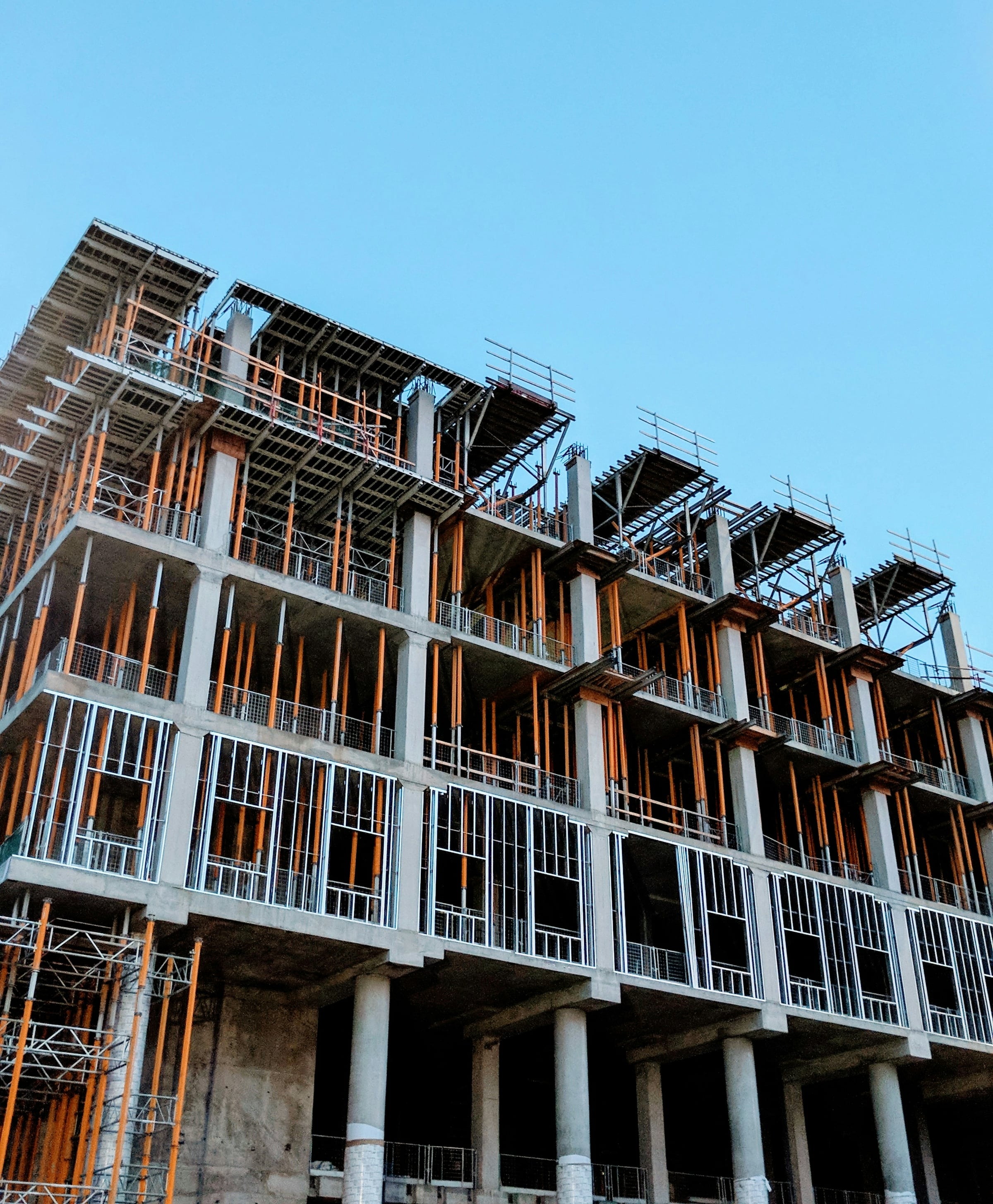 Multi-story apartment building under construction with exposed framing and balconies against a blue sky