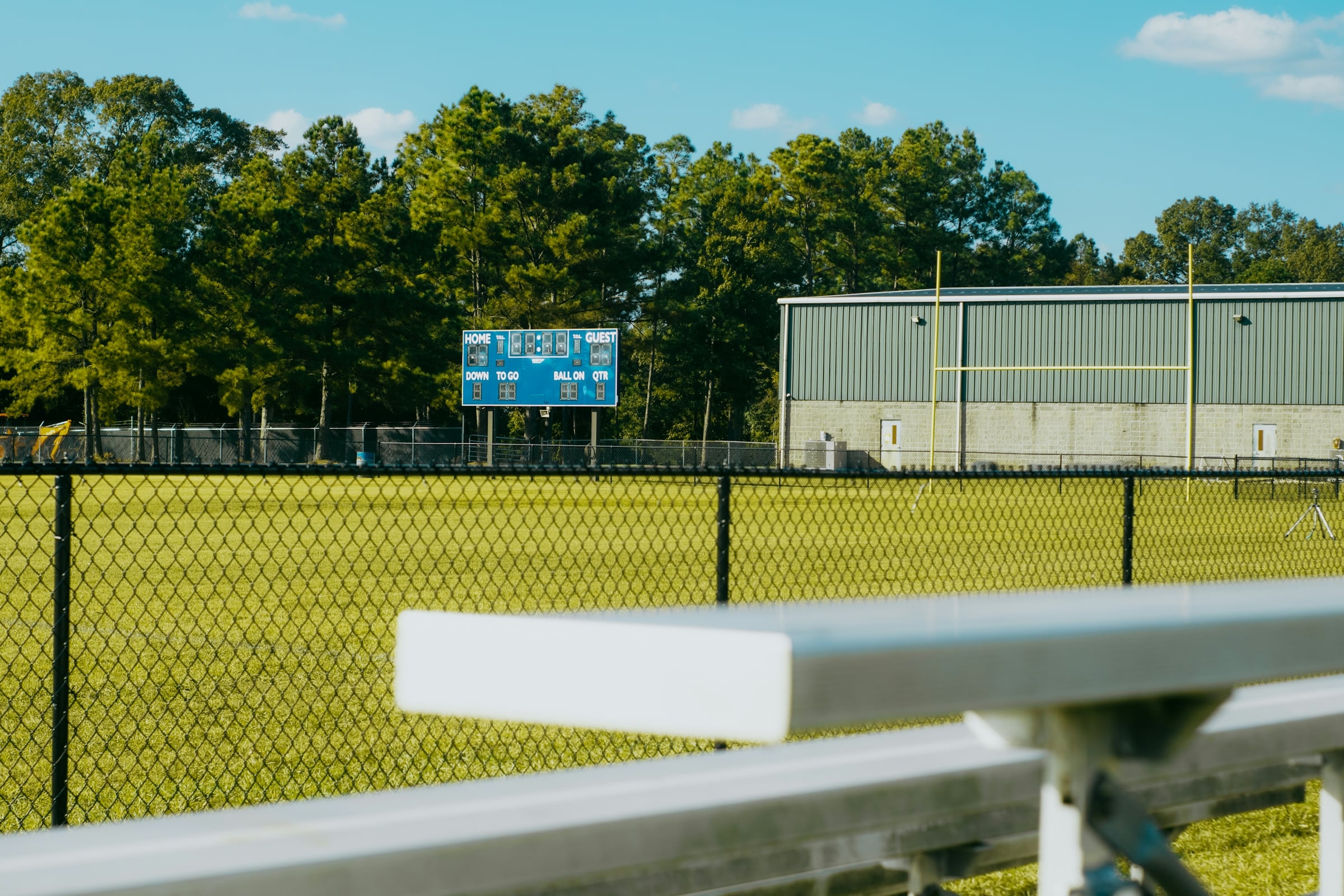 Baseball field with a metal bench, chain link fence and trees on a sunny day