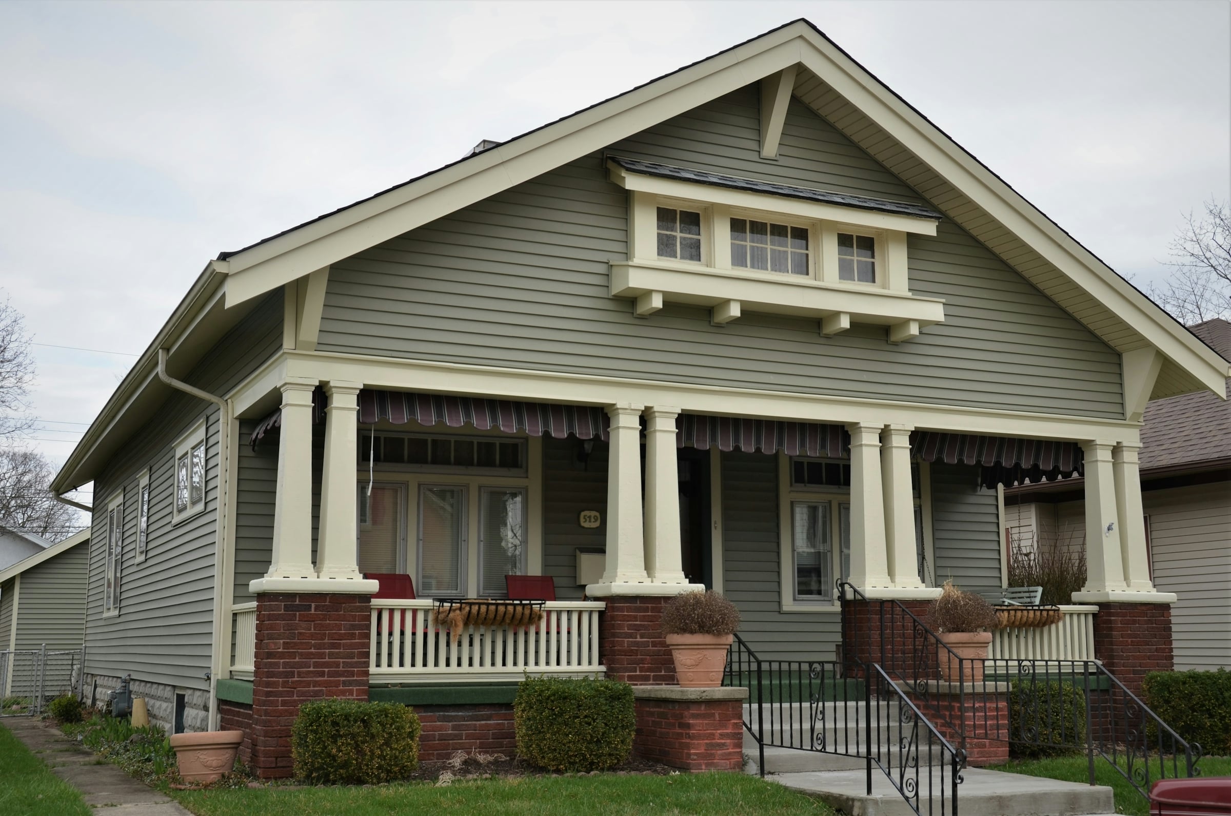 A craftsman-style bungalow with a wide gabled porch, white columns on brick bases and a gray front