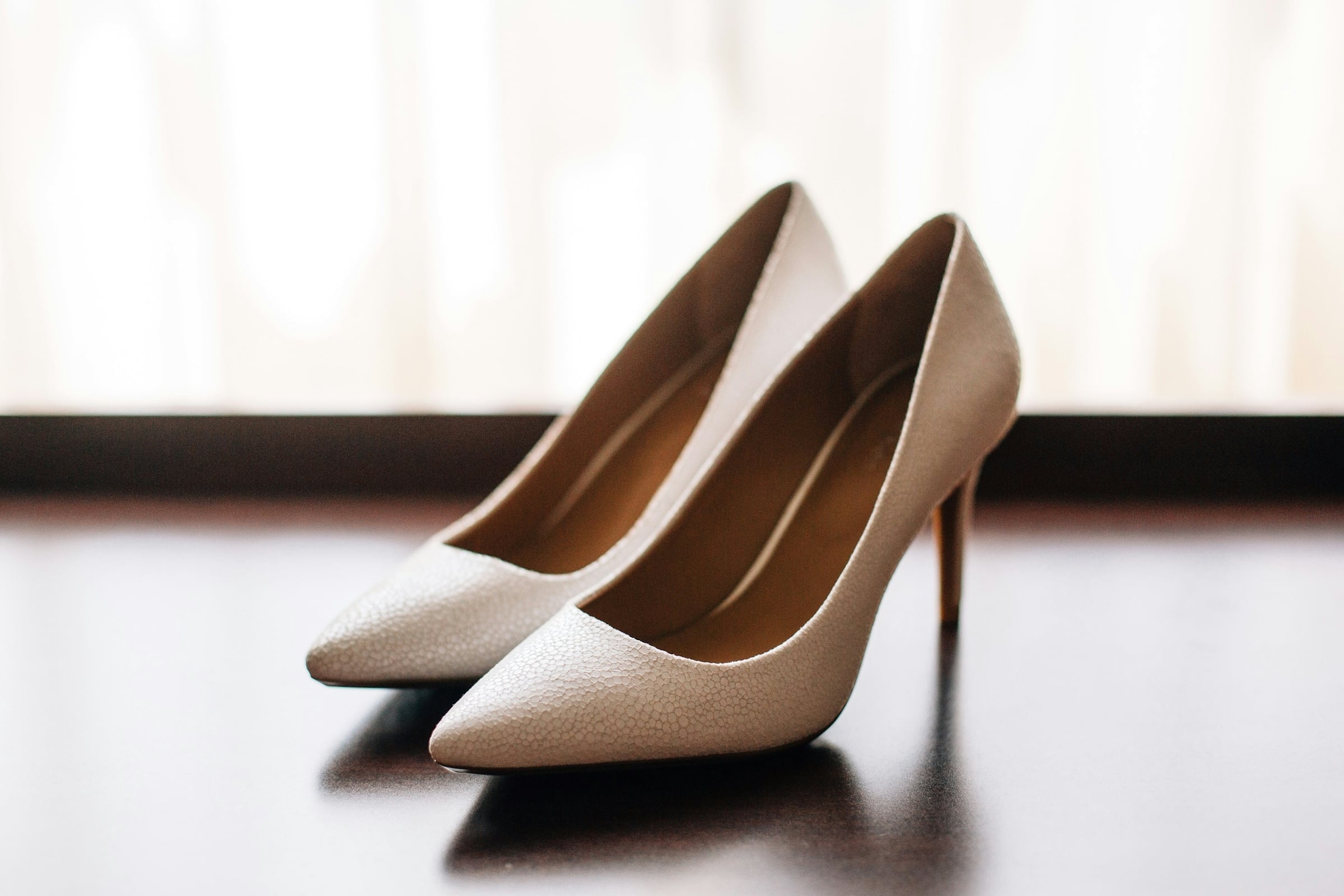 Pair of cream colored high heel pumps on a dark surface