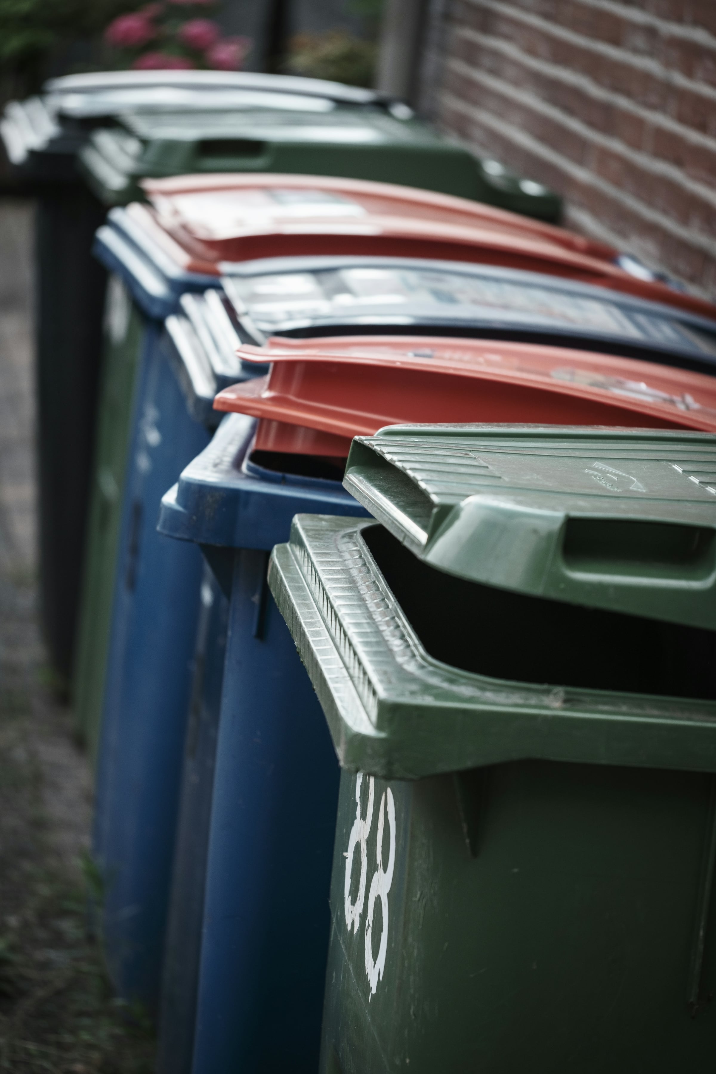 Close view of lidded green, blue and red wheeled trash and recycling carts lined up together
