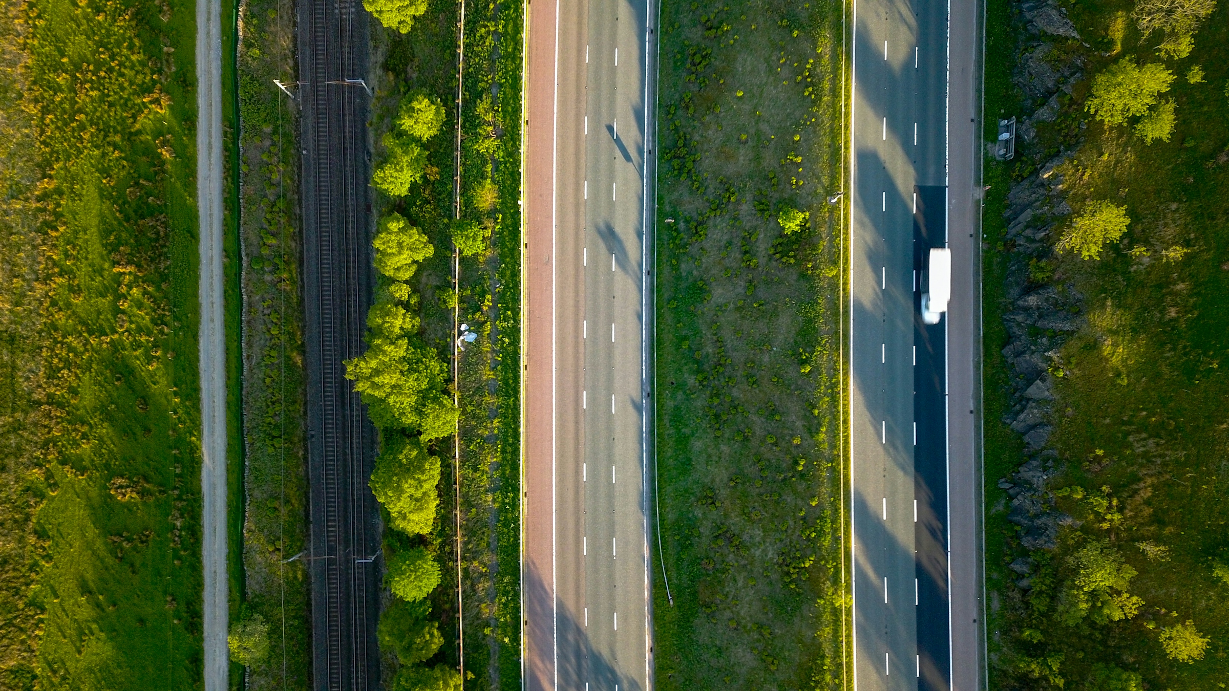 Overhead view of a paved two-direction road with lane markings running between green trees and grass