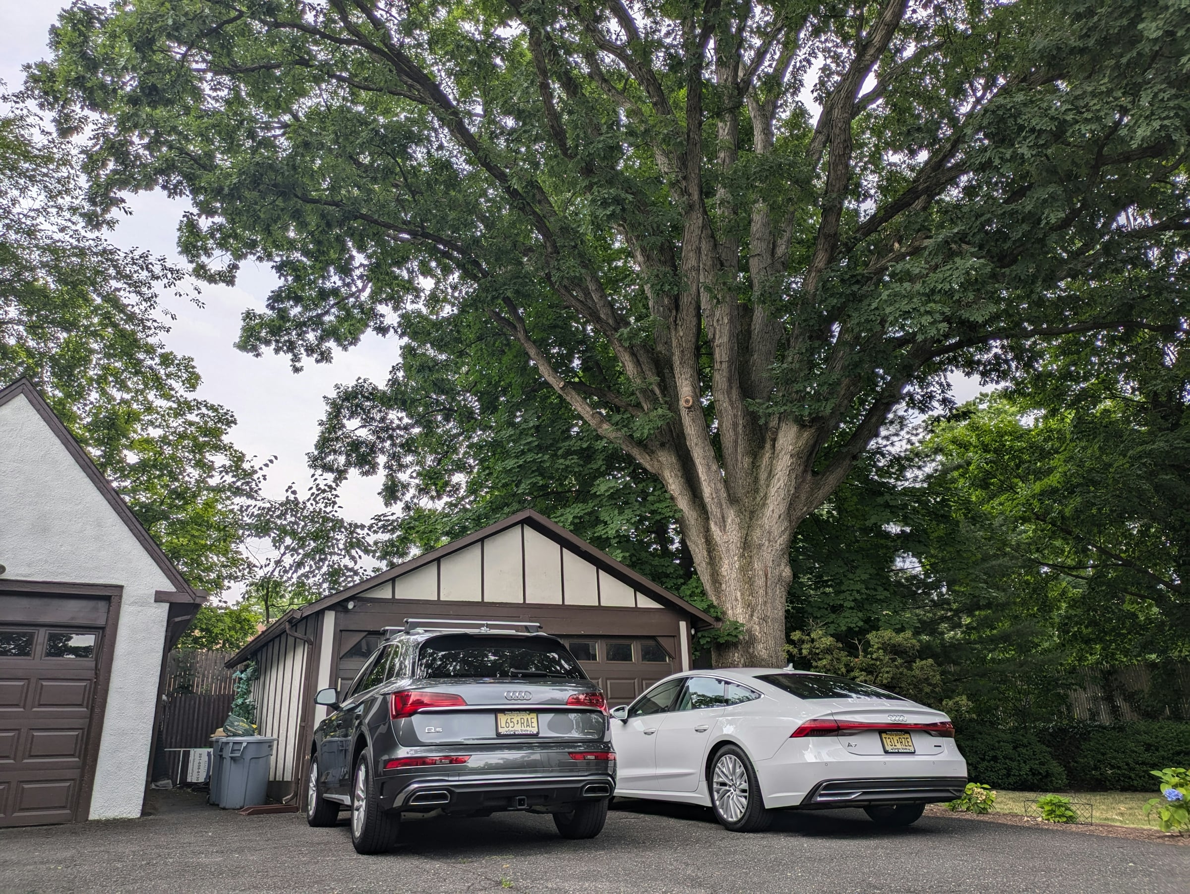 Two cars parked in a gravel driveway beside a detached garage under a large oak tree