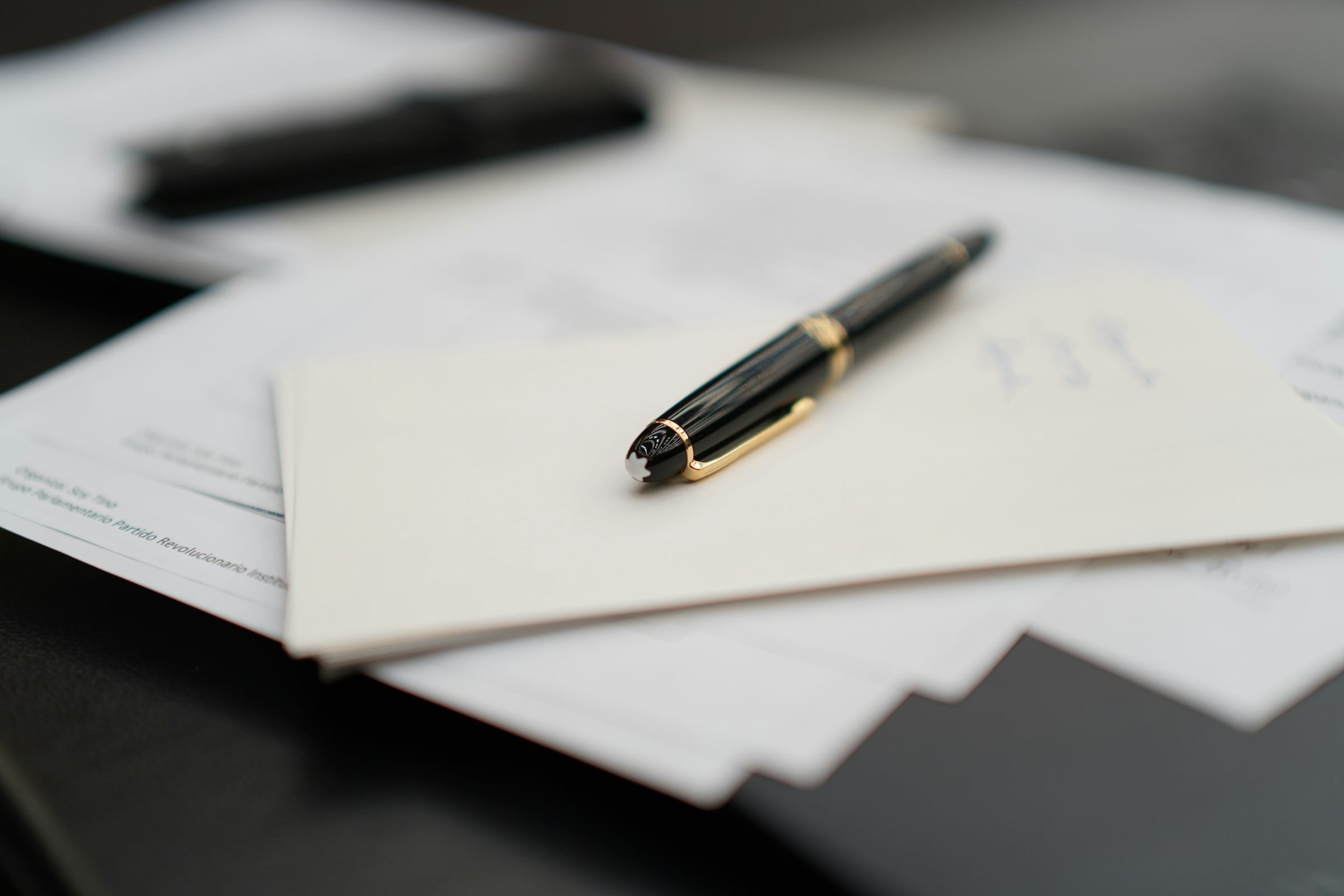 Black fountain pen resting on an envelope and loose legal papers on a dark desk