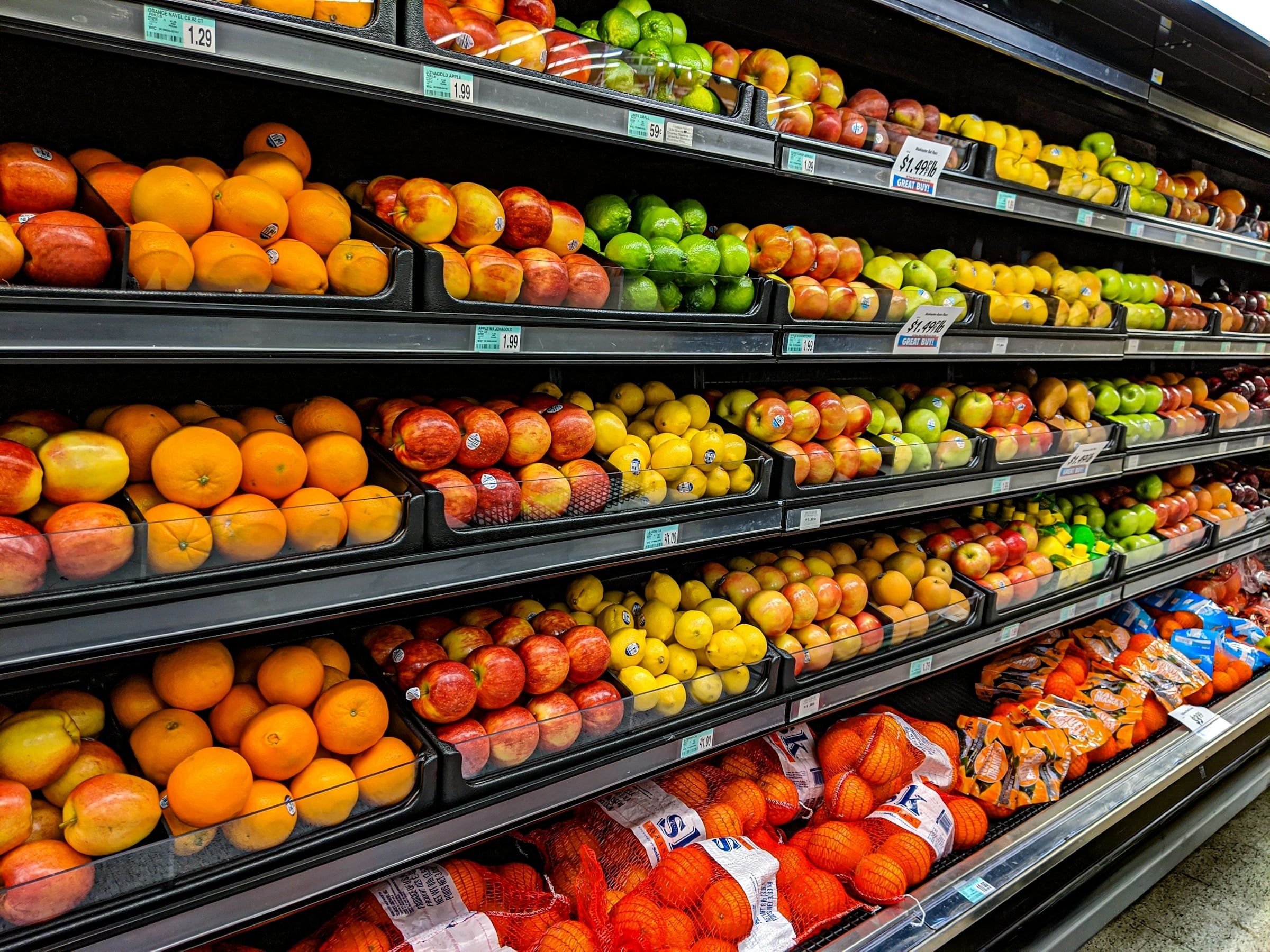 Shelves of oranges, lemons and other fresh produce stacked in rows in a grocery store aisle