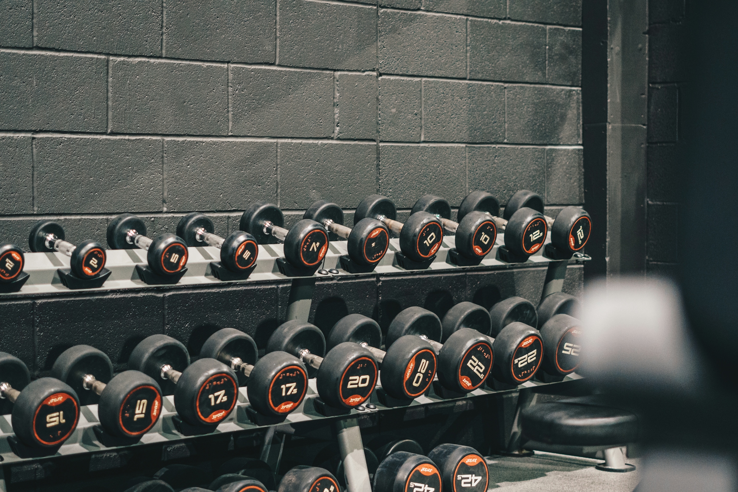 Rows of rubber-coated dumbbells on a rack against a cinder block wall in a gym weight room