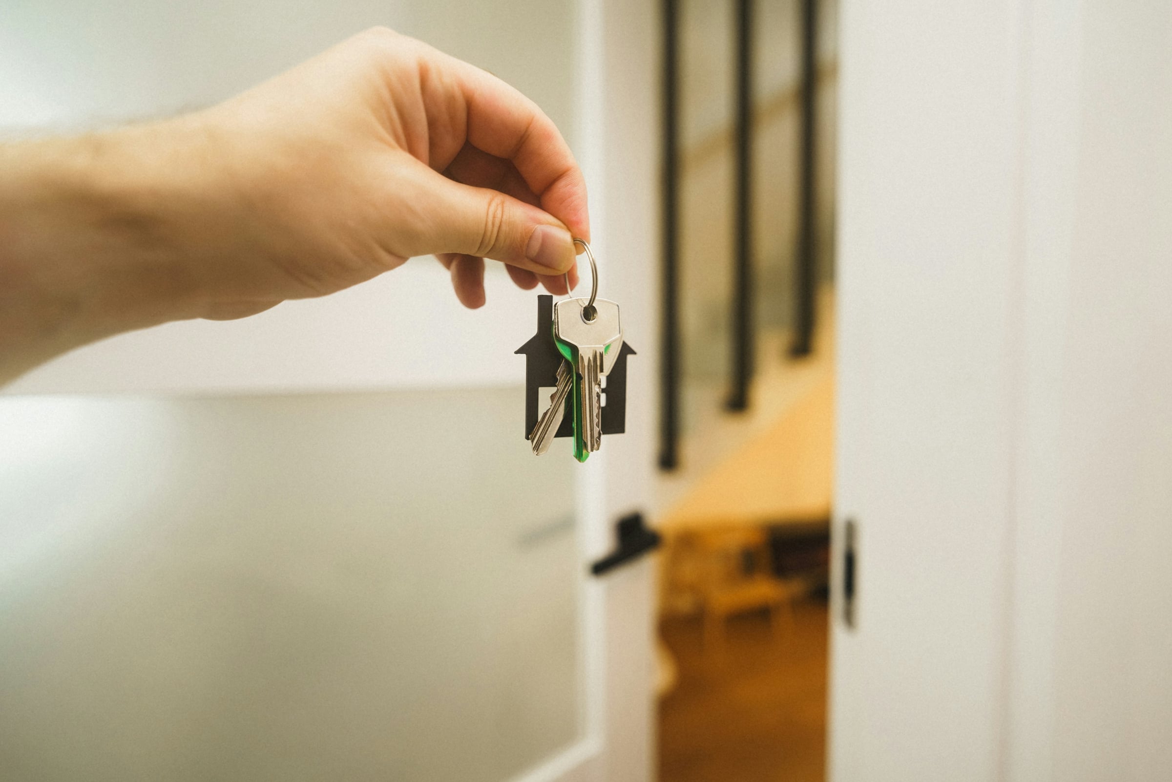 Hand holding a set of keys on a house-shaped keychain in front of an open interior door