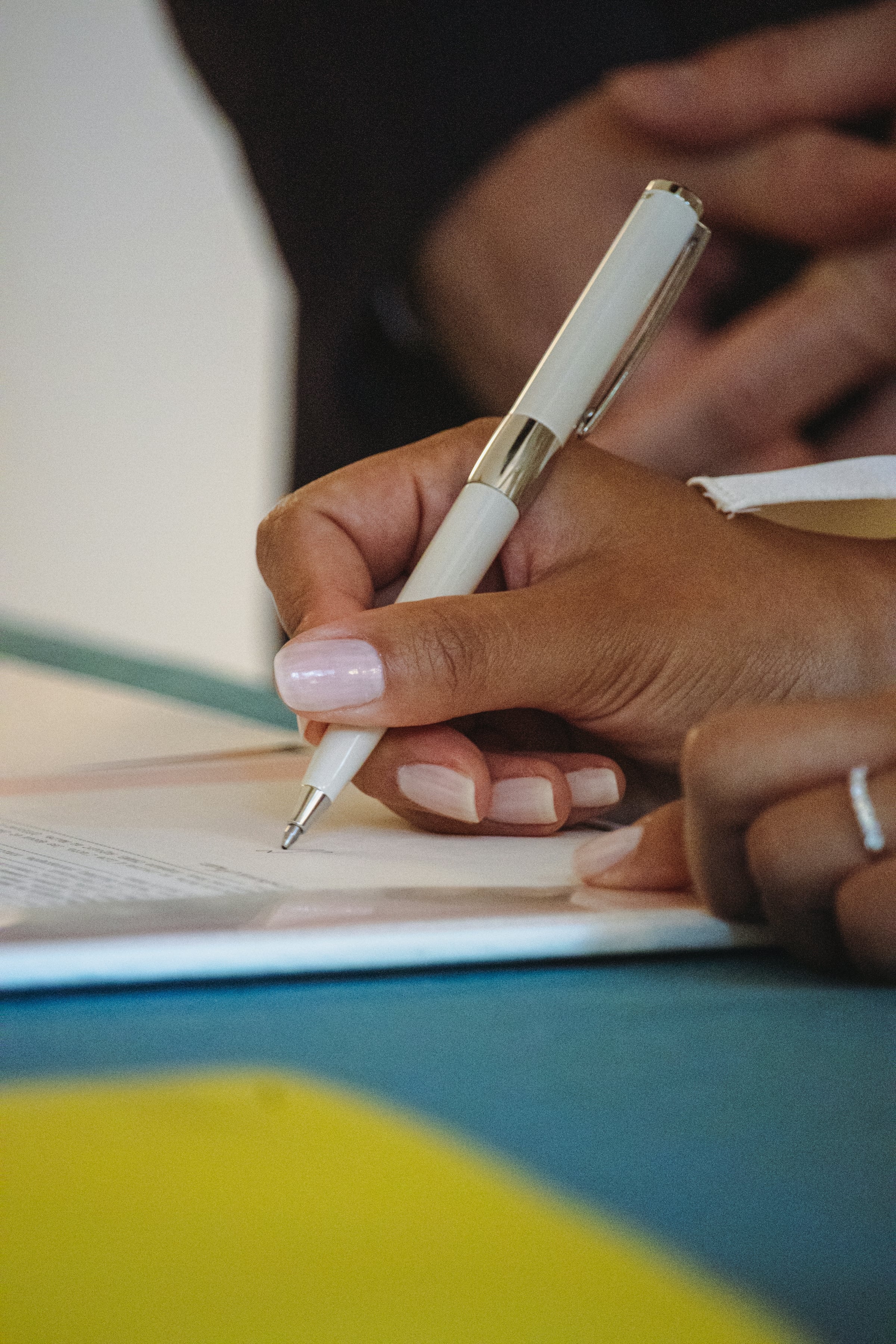 Hand holding a white pen signing a paper document on a desk