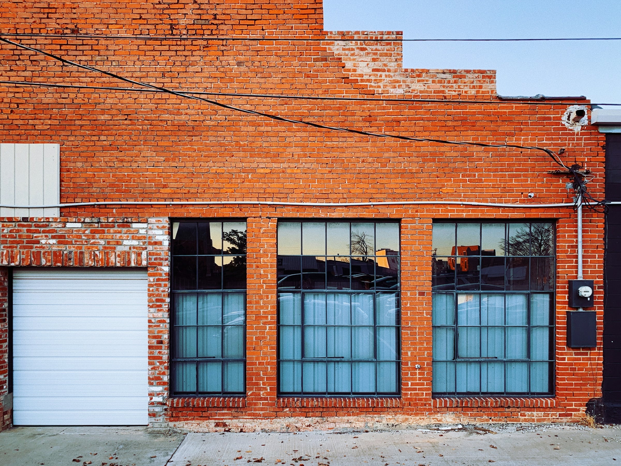 Red brick warehouse building with large industrial windows and a roll-up garage door