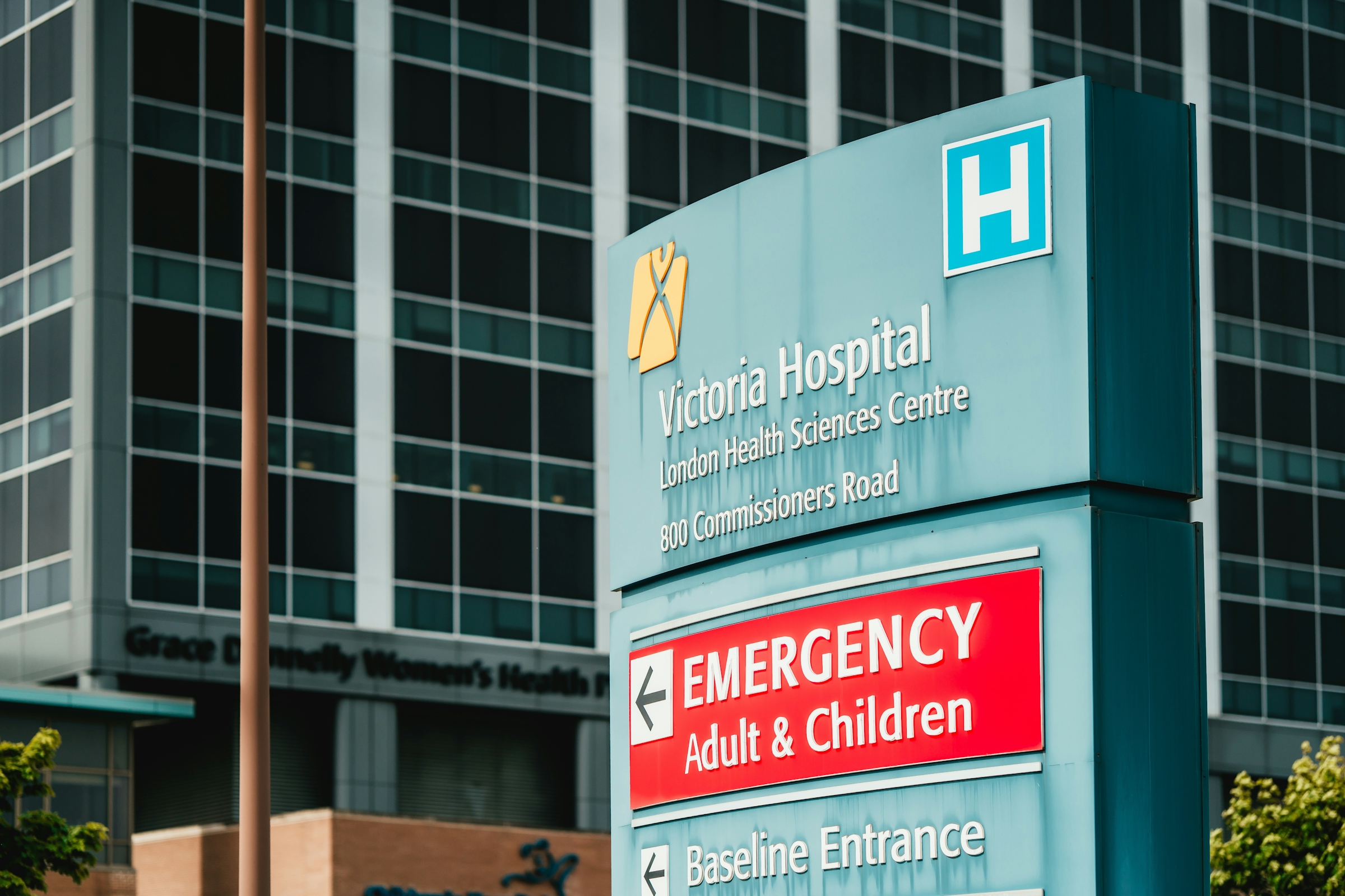 Multistory hospital building with gray paneled walls, a glass facade and a curved brick-and-glass entrance beneath a blue sky with clouds