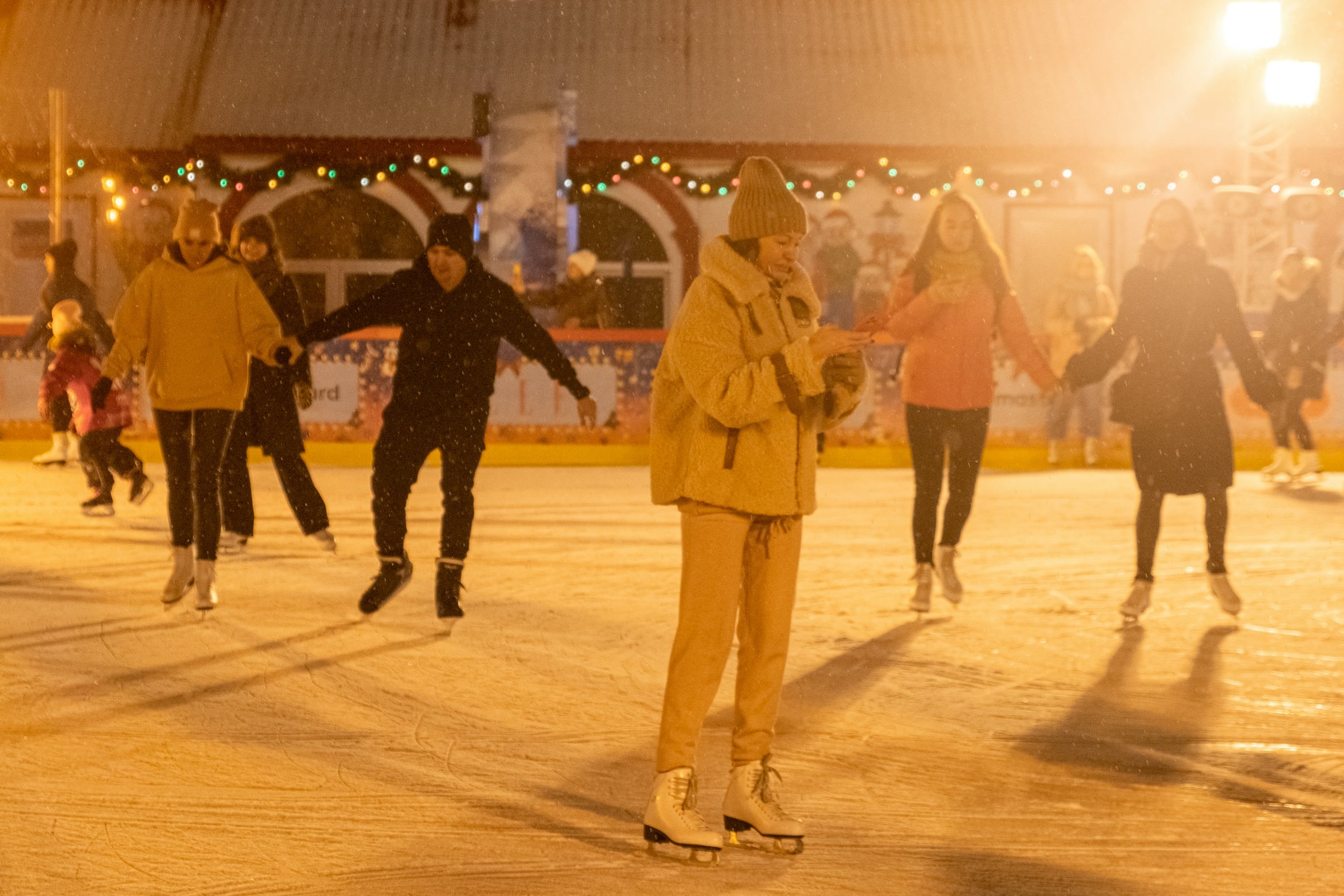 Ice skaters gliding across an outdoor rink in warm evening light