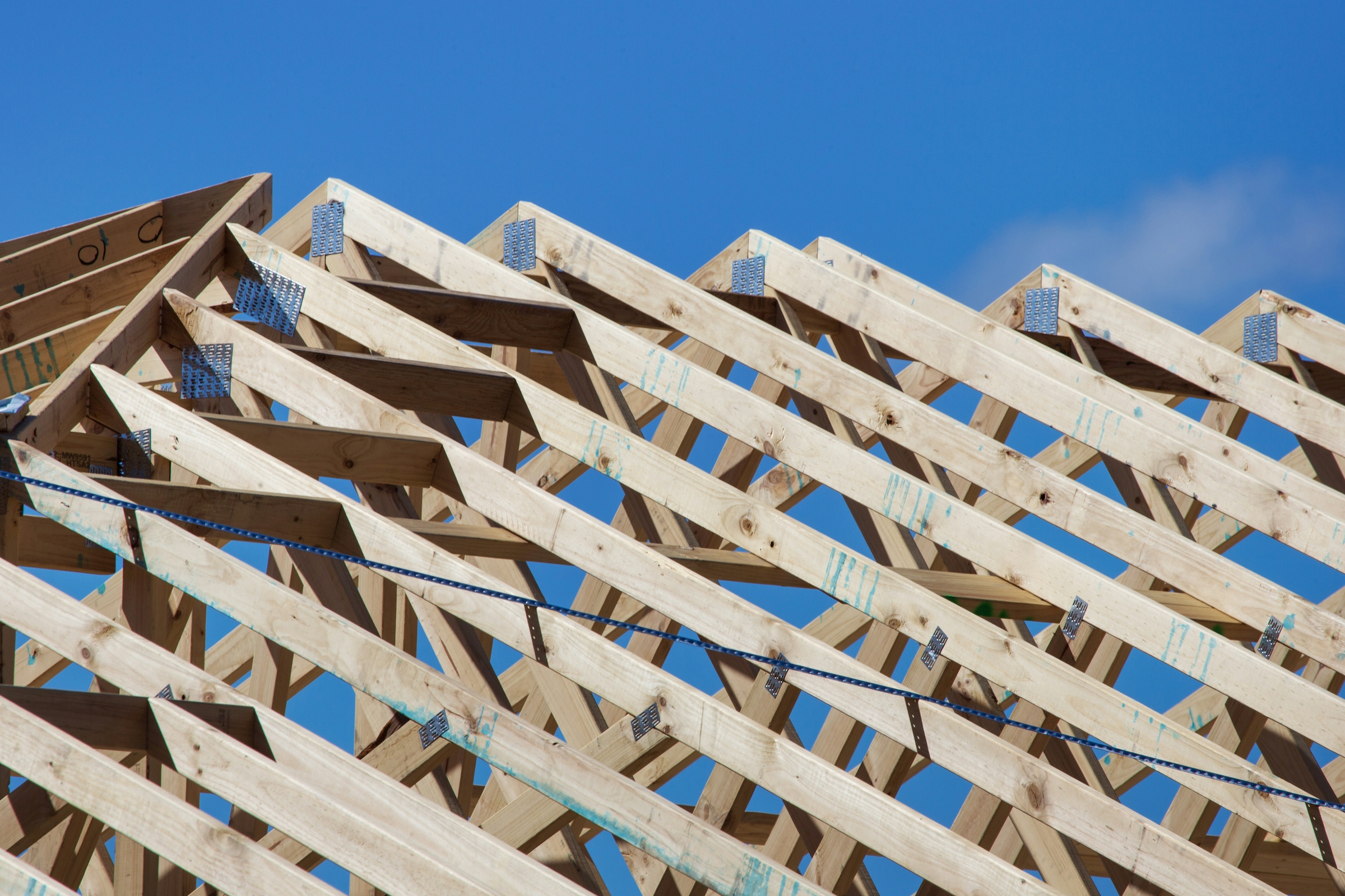 Wooden roof trusses and rafters of a house under construction against a clear blue sky
