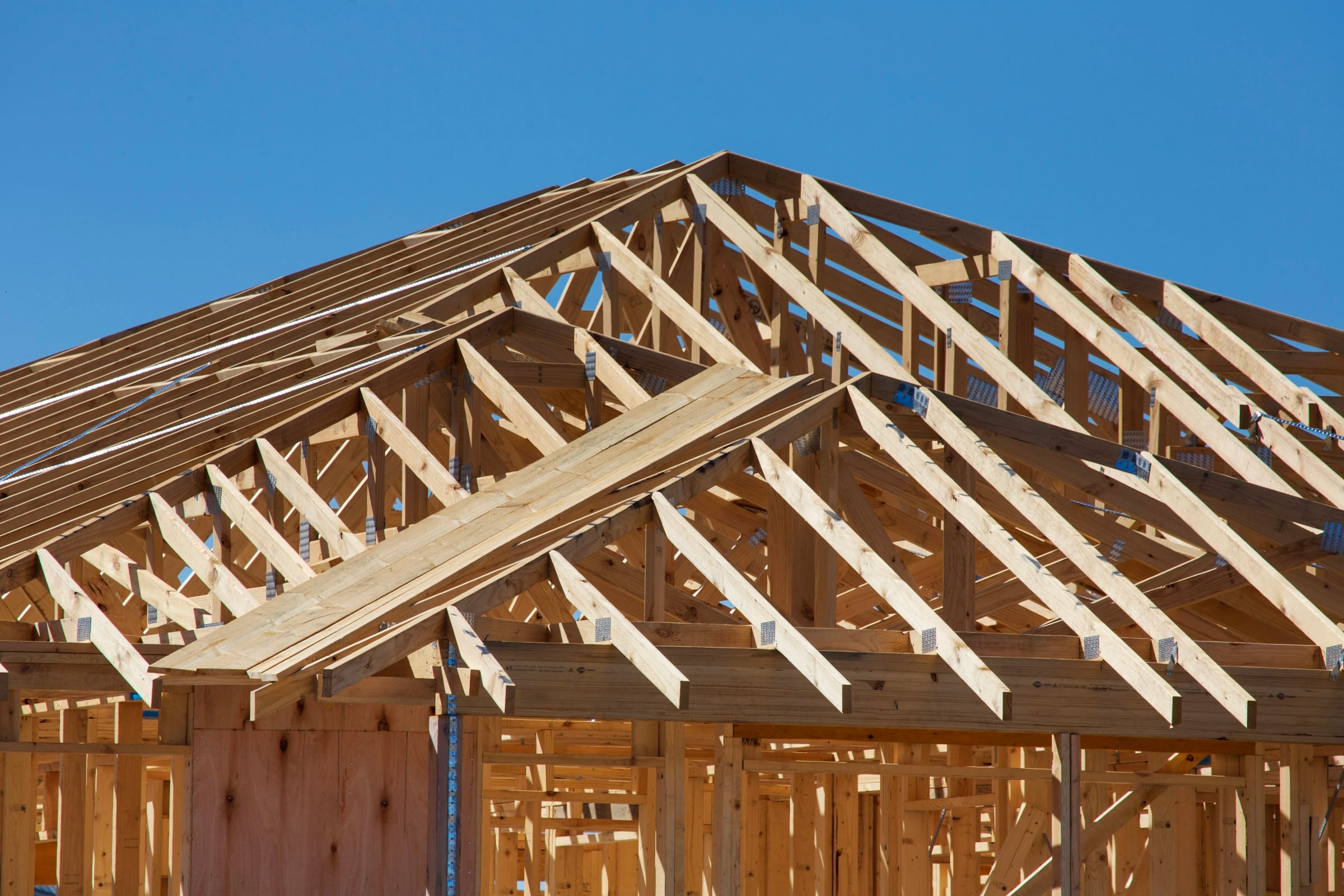 Wood roof trusses and wall framing on a new house under construction against a blue sky