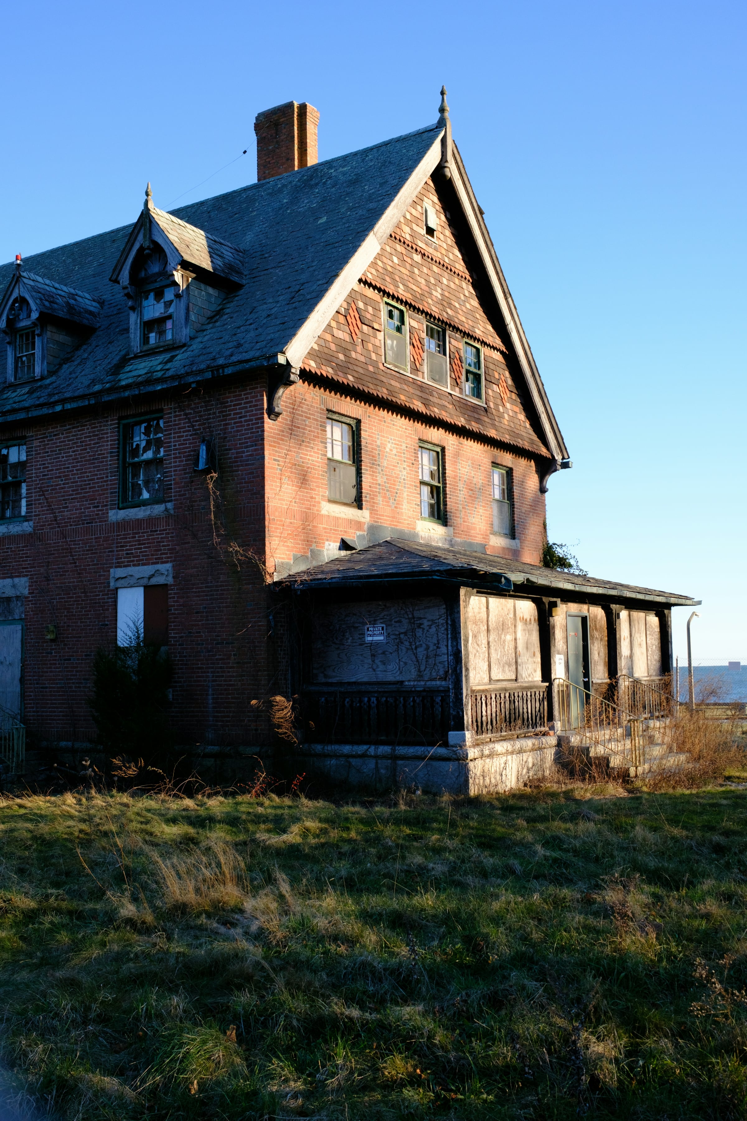 Weathered red brick house with a dark shingled roof and a worn wooden front porch, ready for restoration