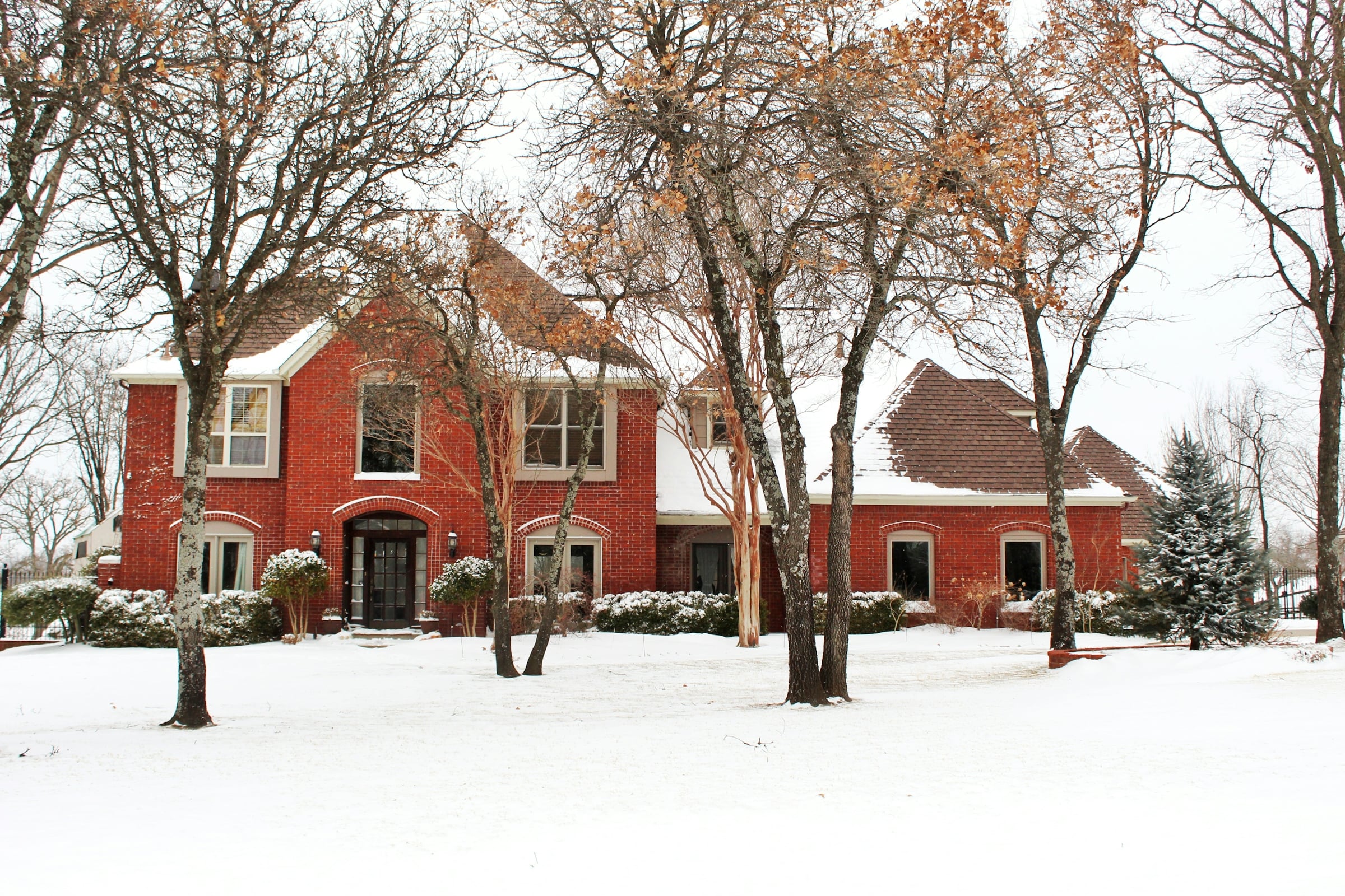 Red brick two-story house with a snow-covered lawn and bare trees in winter