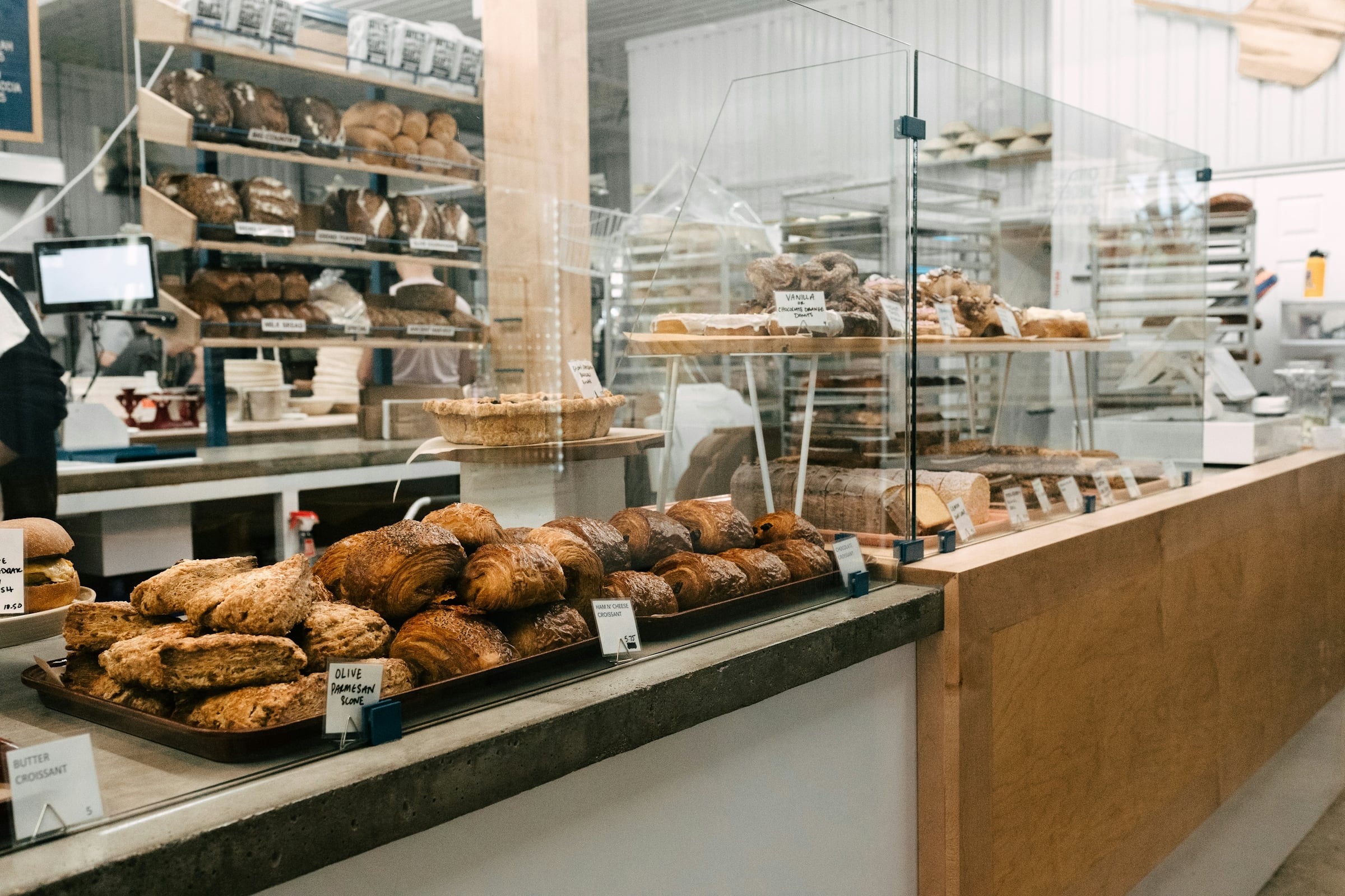 A bakery counter with trays of baked pastries and loaves of bread behind a glass divider