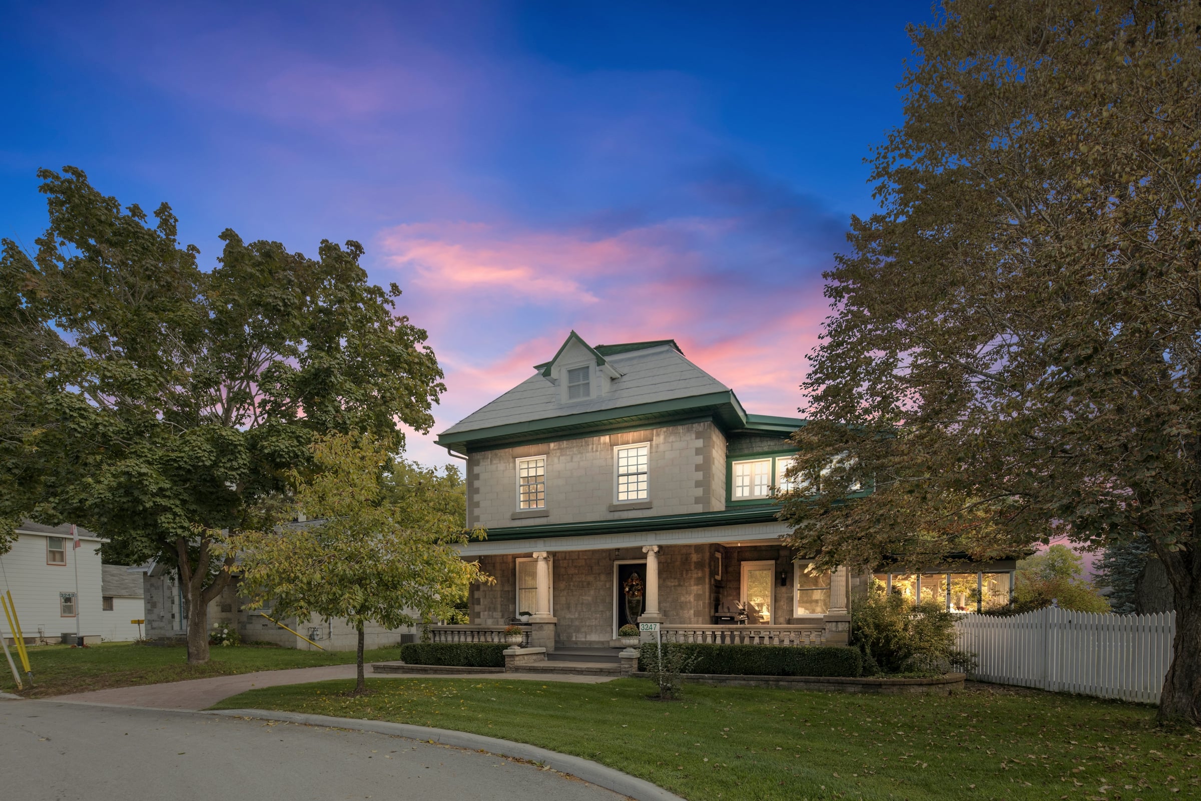 Two-story house with a covered front porch and a green lawn at dusk under a pink and blue sky
