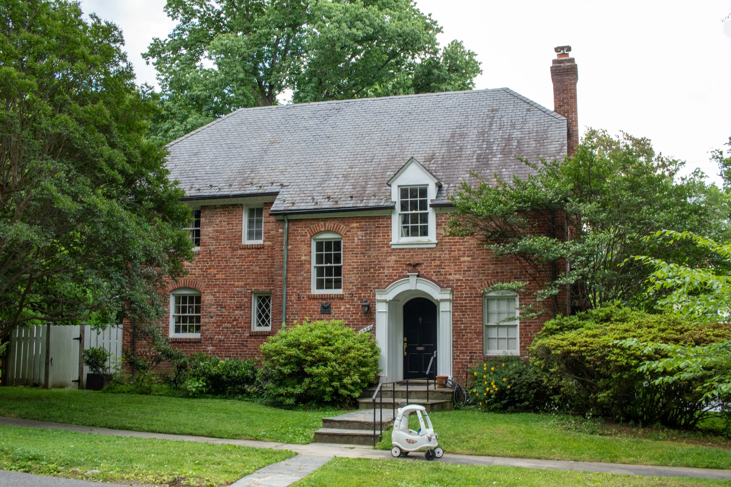 Red brick two-story house with a white arched doorway and mature trees around the front yard
