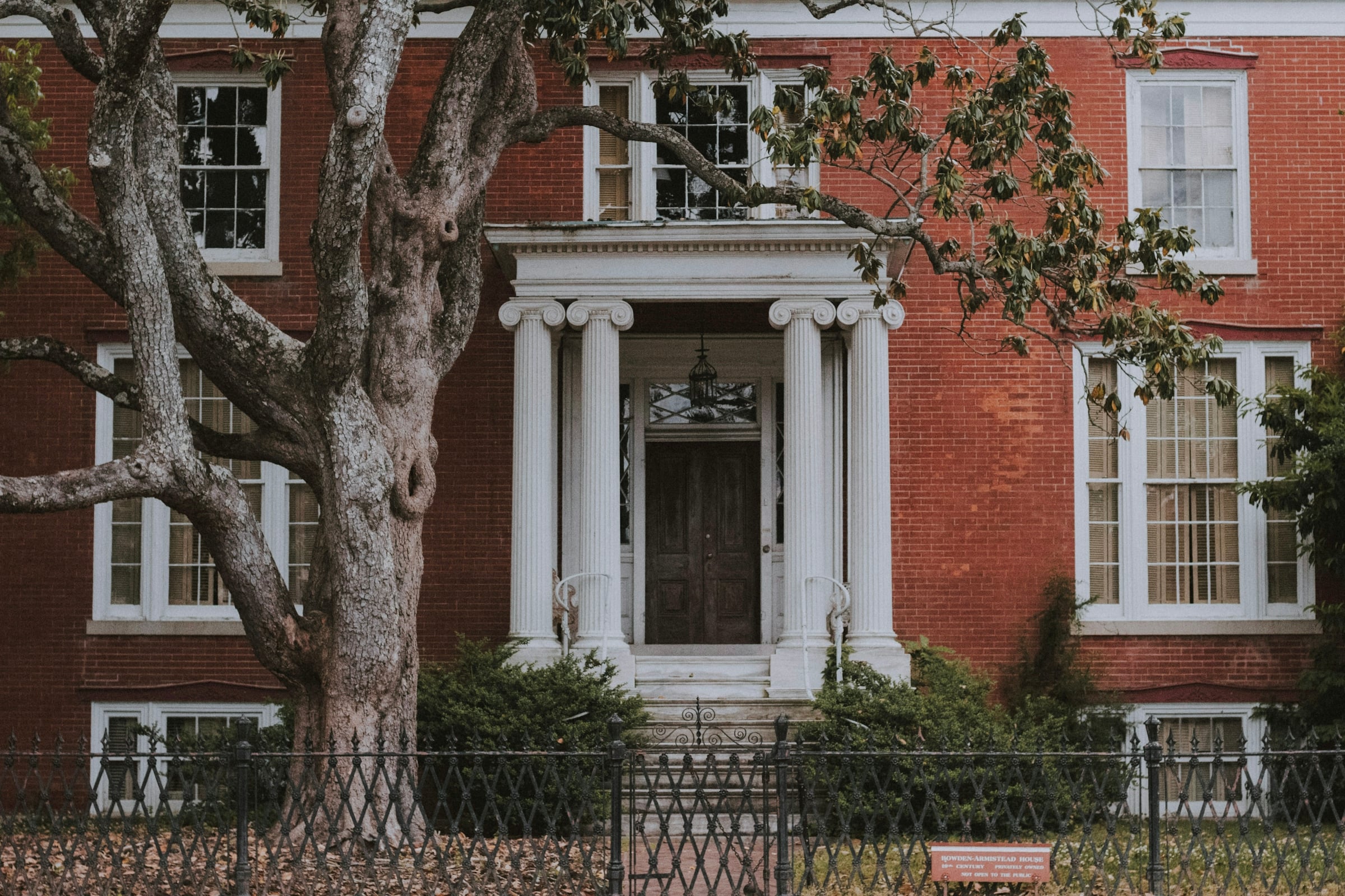 Red brick Georgian-style house entrance with white columns and a large bare-limbed tree in front