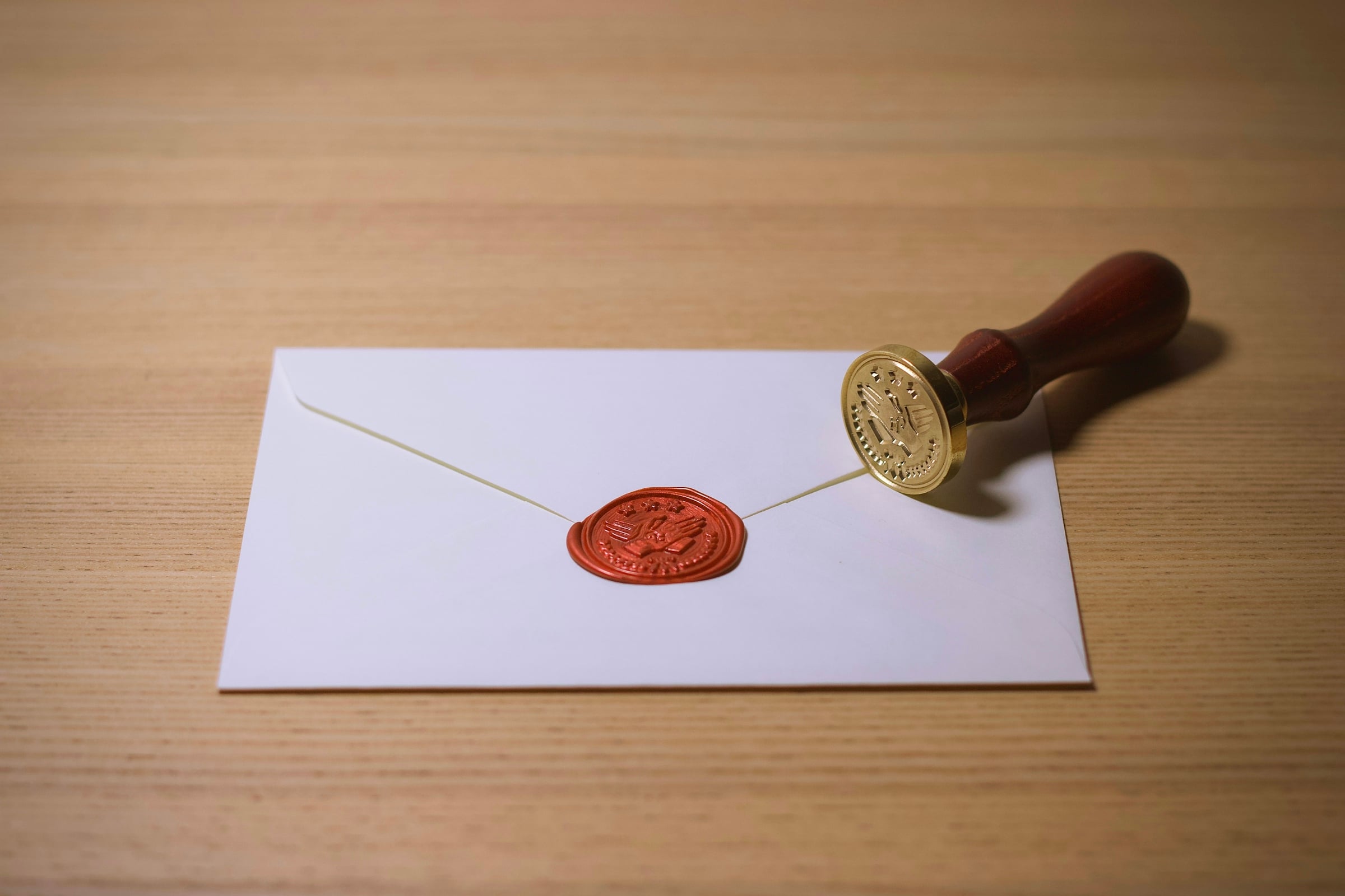 A brass-handled wax seal stamp resting beside a white envelope sealed with red wax on a wooden desk