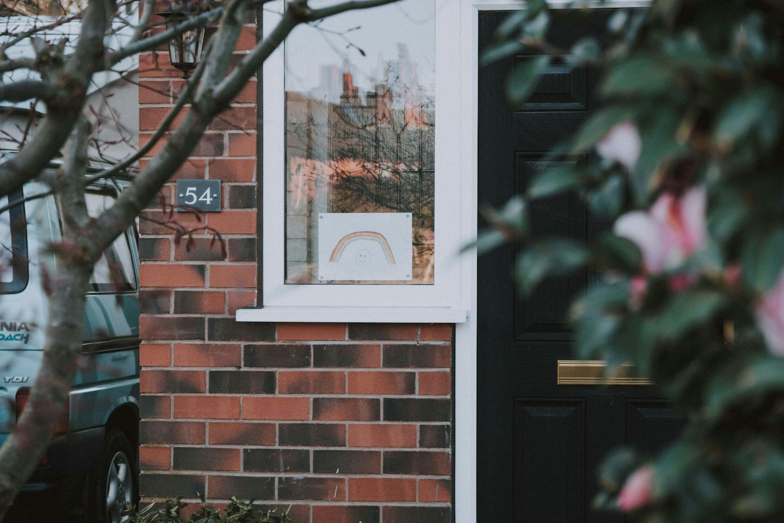 Red brick house front with a white-framed window, black front door and flowering branches