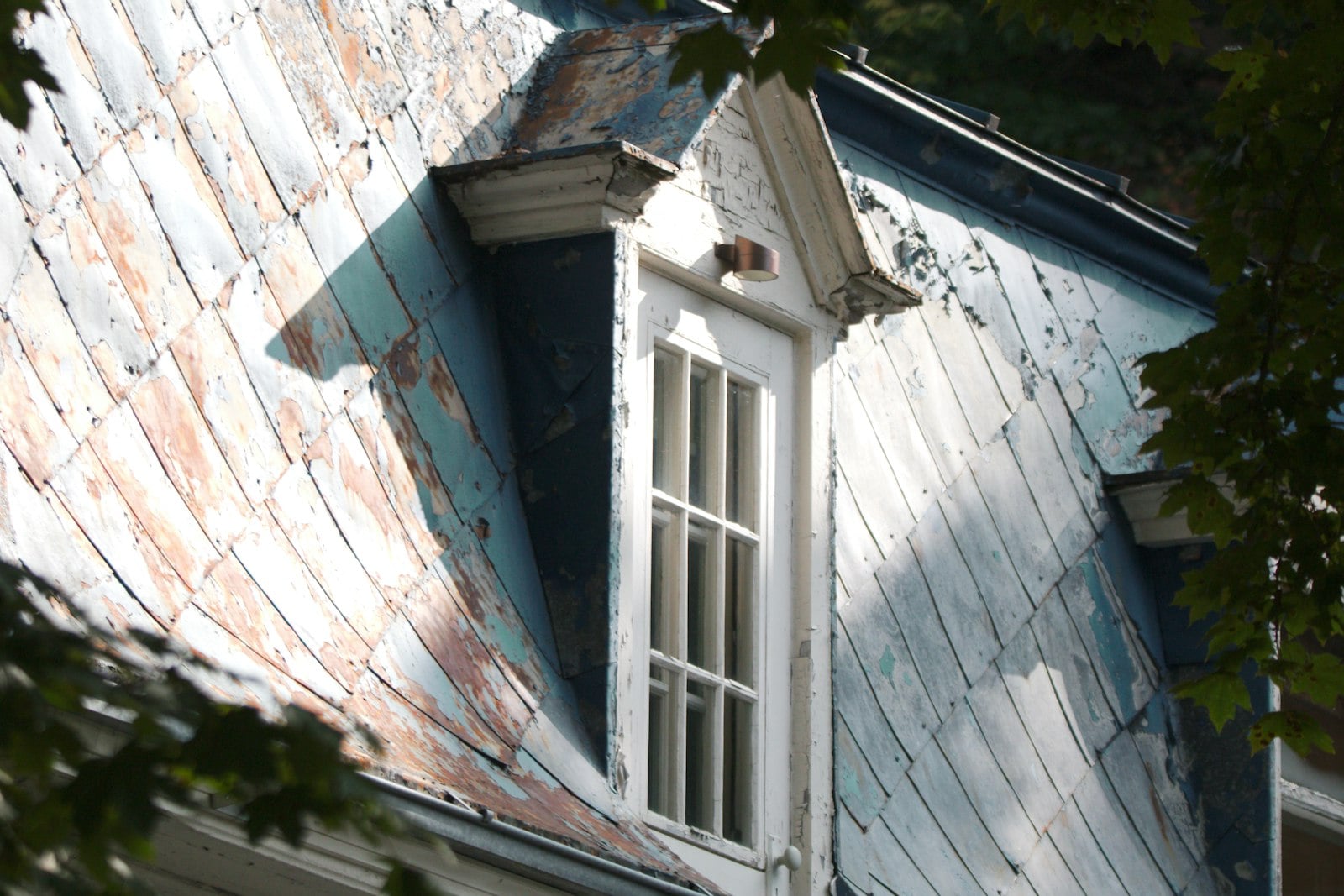 Weathered slate-shingled roof with a dormer window on an older house