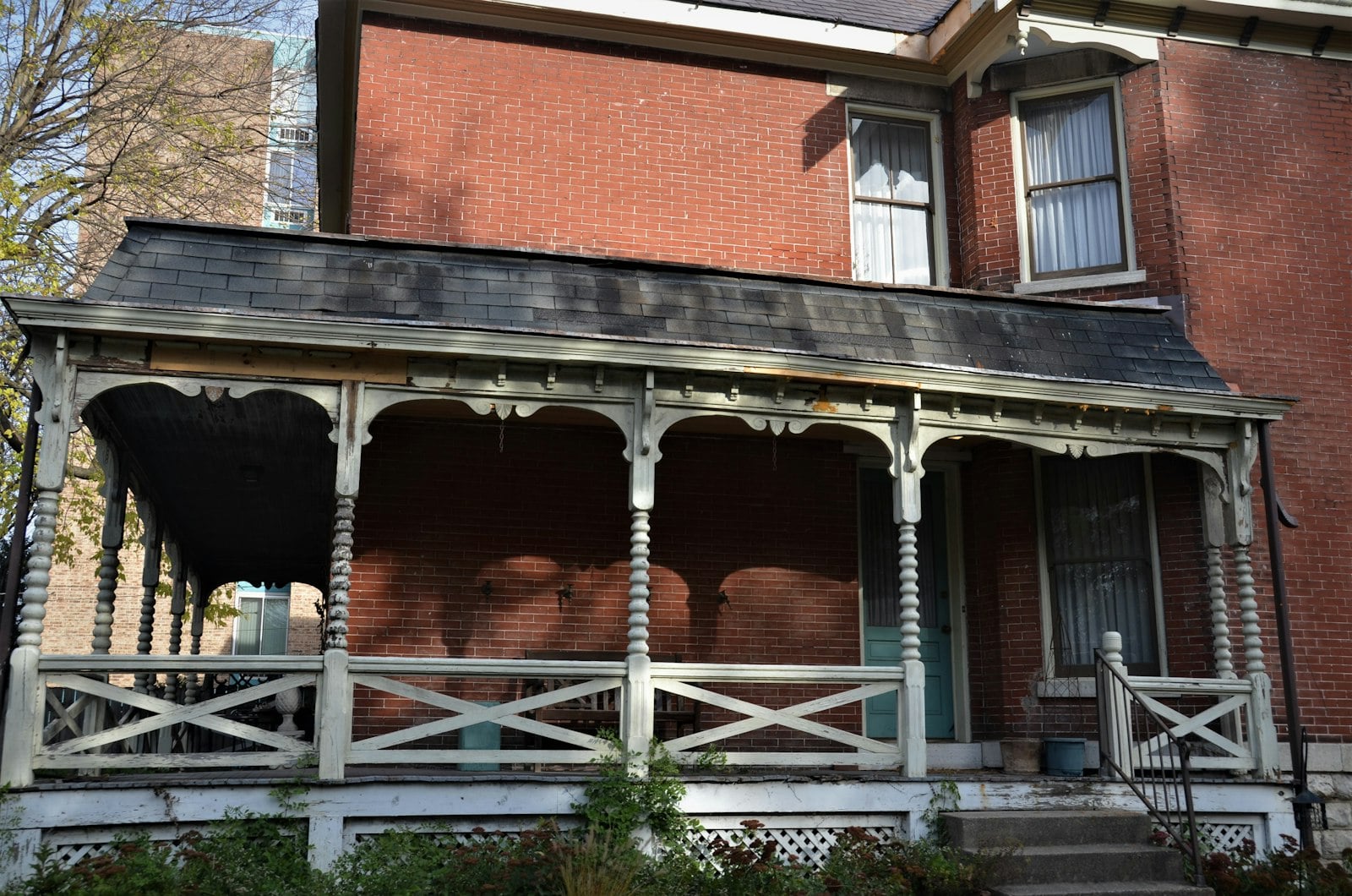 Red brick house with a Victorian-style wood porch with turned posts and a slate-shingled roof