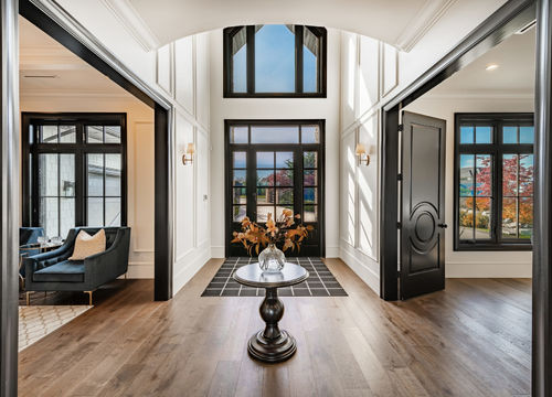 stately luxurious elegant entry hall foyer welcome front door with glass and large area rug round table with floral flower arrangement white wood panelled walls staircase stairs open concept
