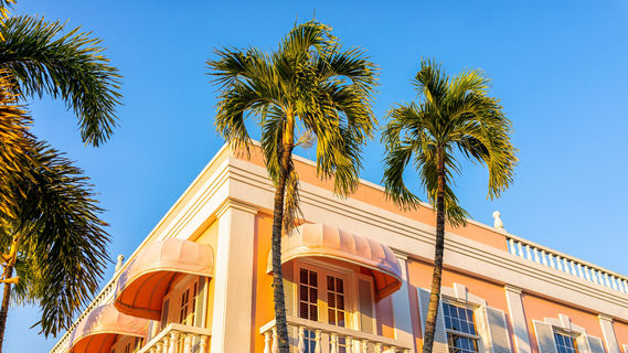 Naples - Old town Naples, Florida downtown on Third Street South shopping district with pink building architecture exterior at sunset with palm trees and baby blue sky