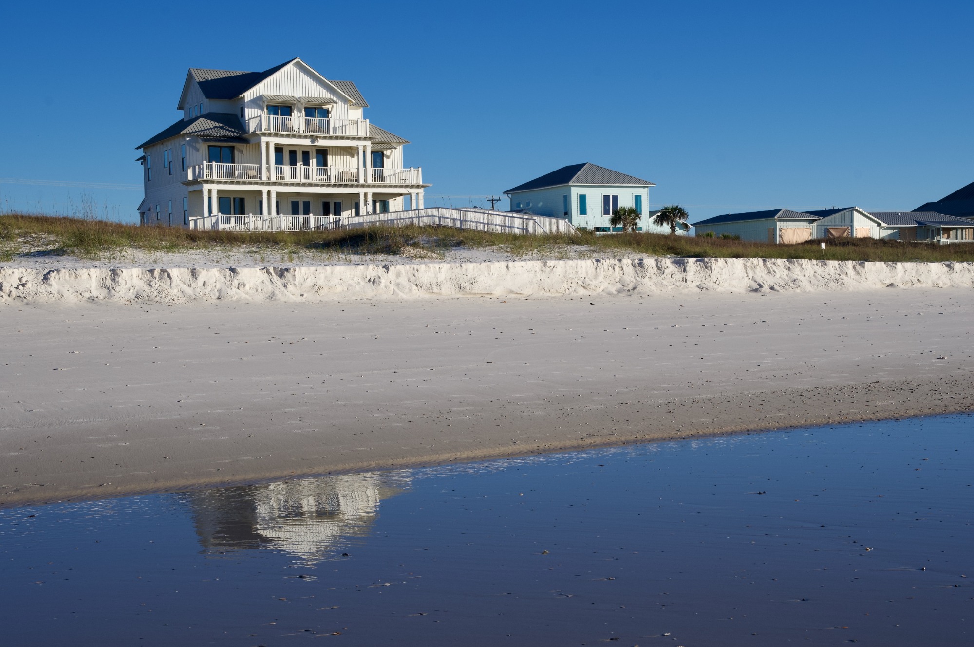 beach houses on the gulf shore of alabama on a sunny day with reflections in the shallow water on shore