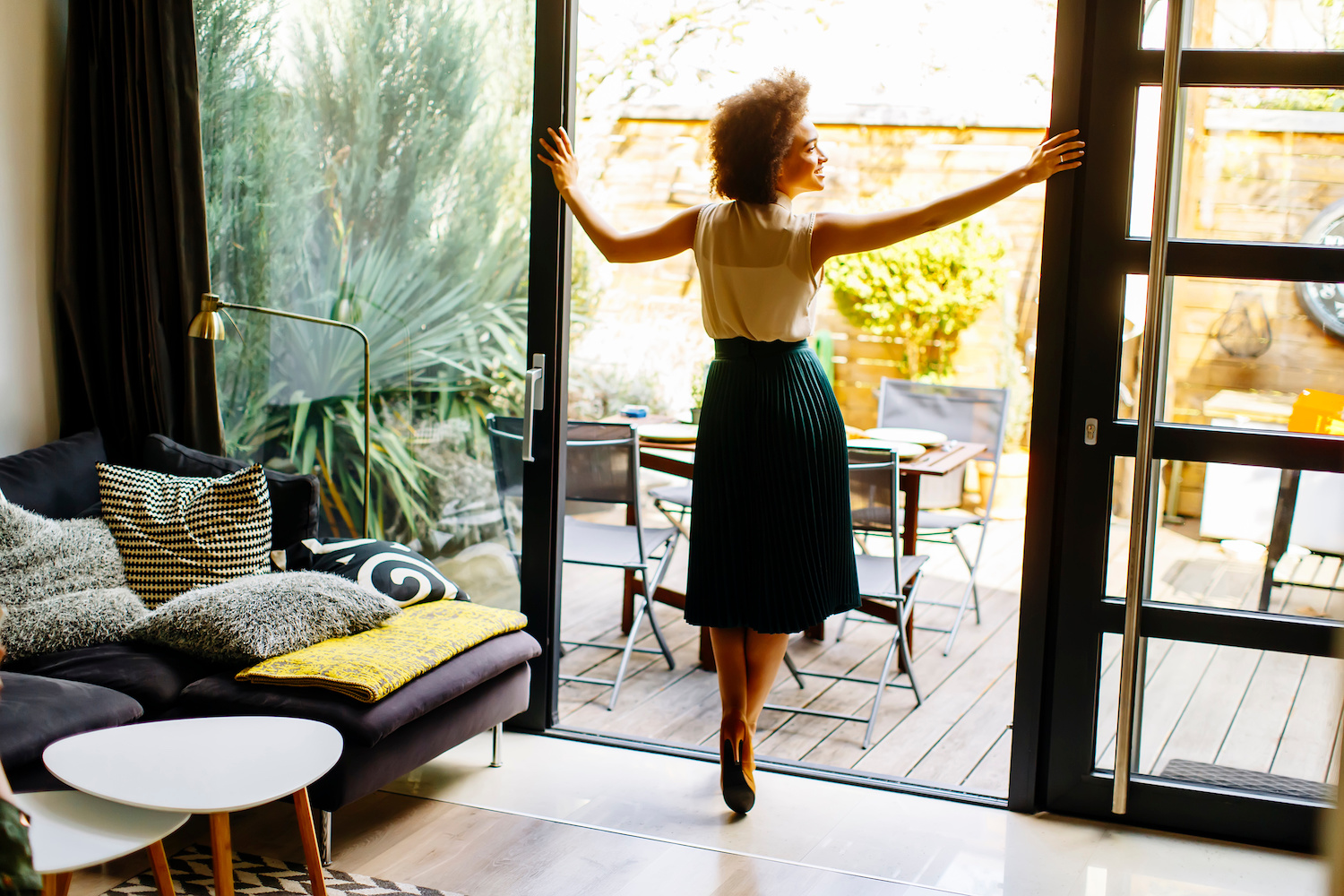 Young woman with curly hair posira in the house next to the open glass door