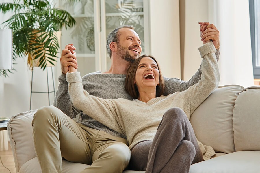 excited-child-free-couple-holding-hands-and-laughing-on-cozy-couch-in-living-room-fun-and-leisure