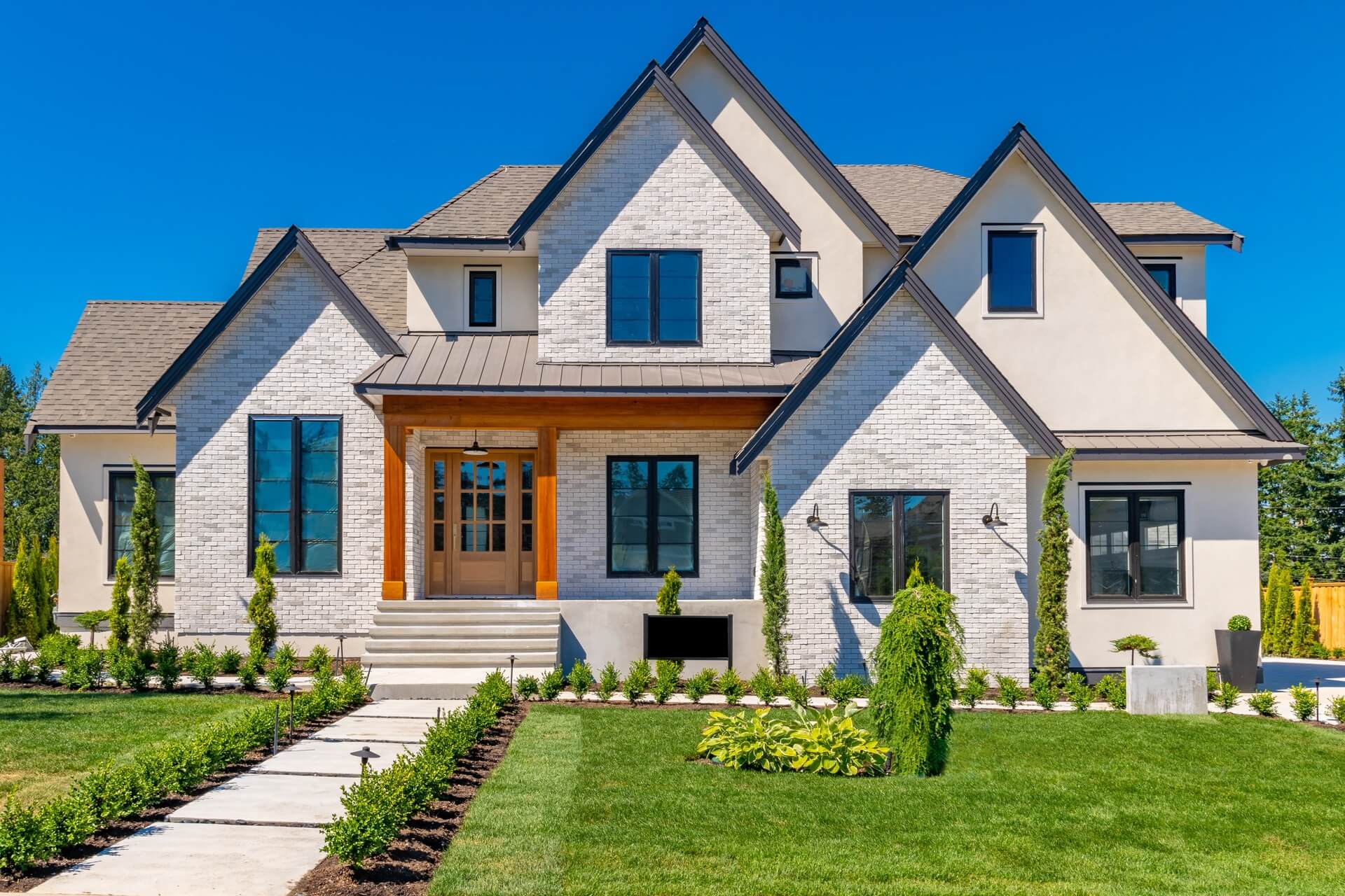 Large estate home with blue sky luxurious landscaping stone brick facade multiple peak roof and windows