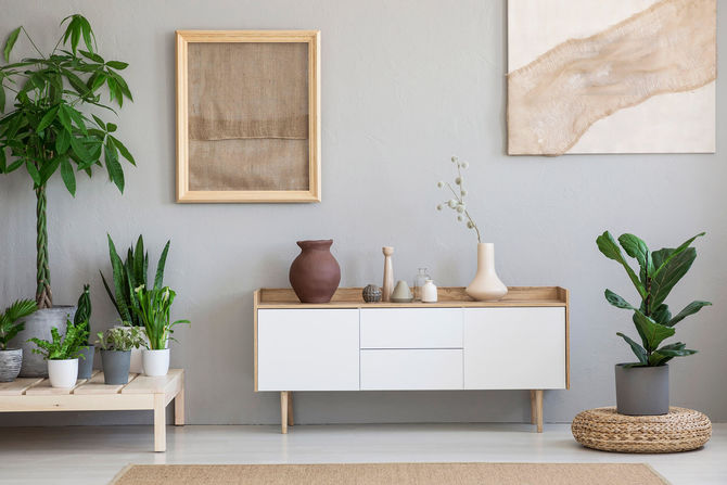 Posters on grey wall above white cupboard in living room interior with plants and pouf. Real photo