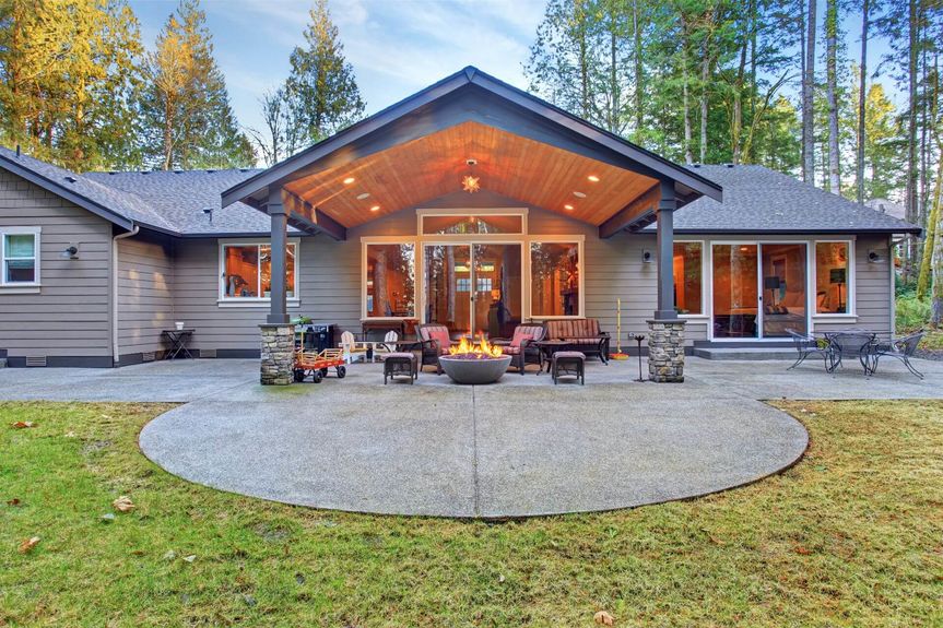 Large back yard with grass and covered patio with fire pit.
