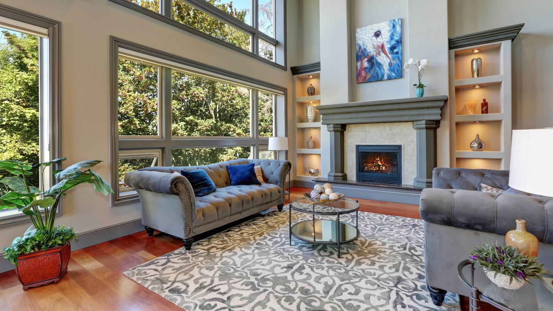 Grey interior of high vaulted ceiling family room in luxury house with fireplace and large windows