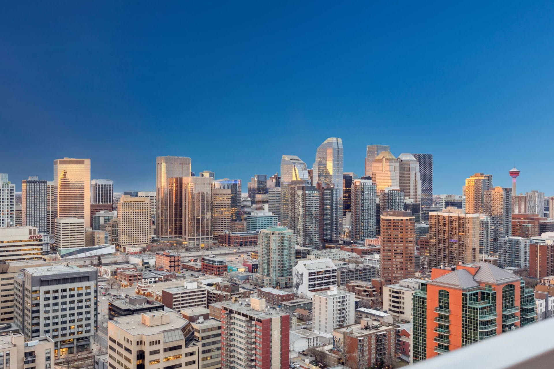 Panoramic view of downtown Calgary, Alberta, featuring modern high-rise buildings and the Calgary Tower under a clear blue evening sky.
